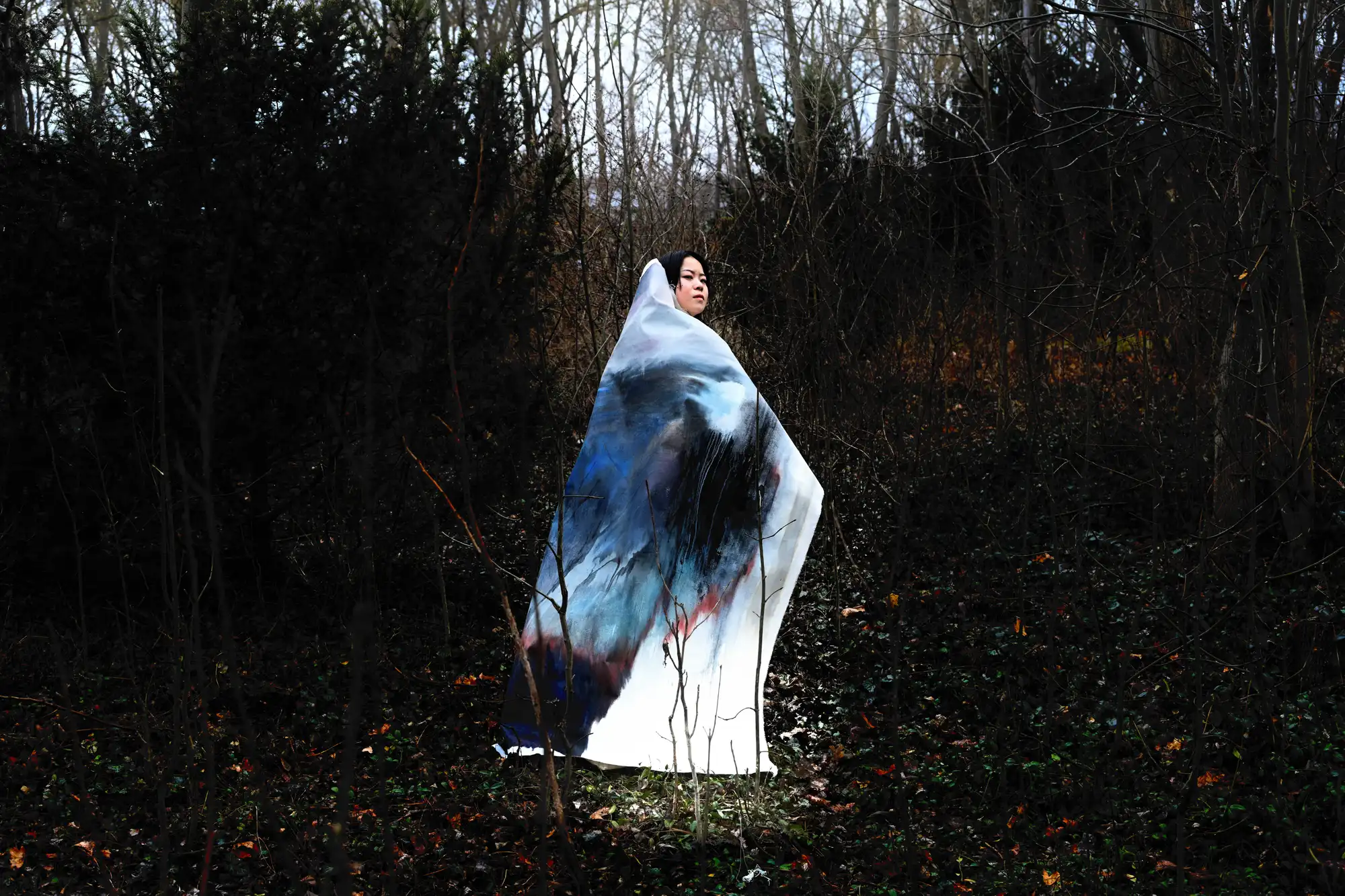 Full-body view of Igigo Wu holding two large paintings during site-specific performance at Zentralfriedhof Vienna