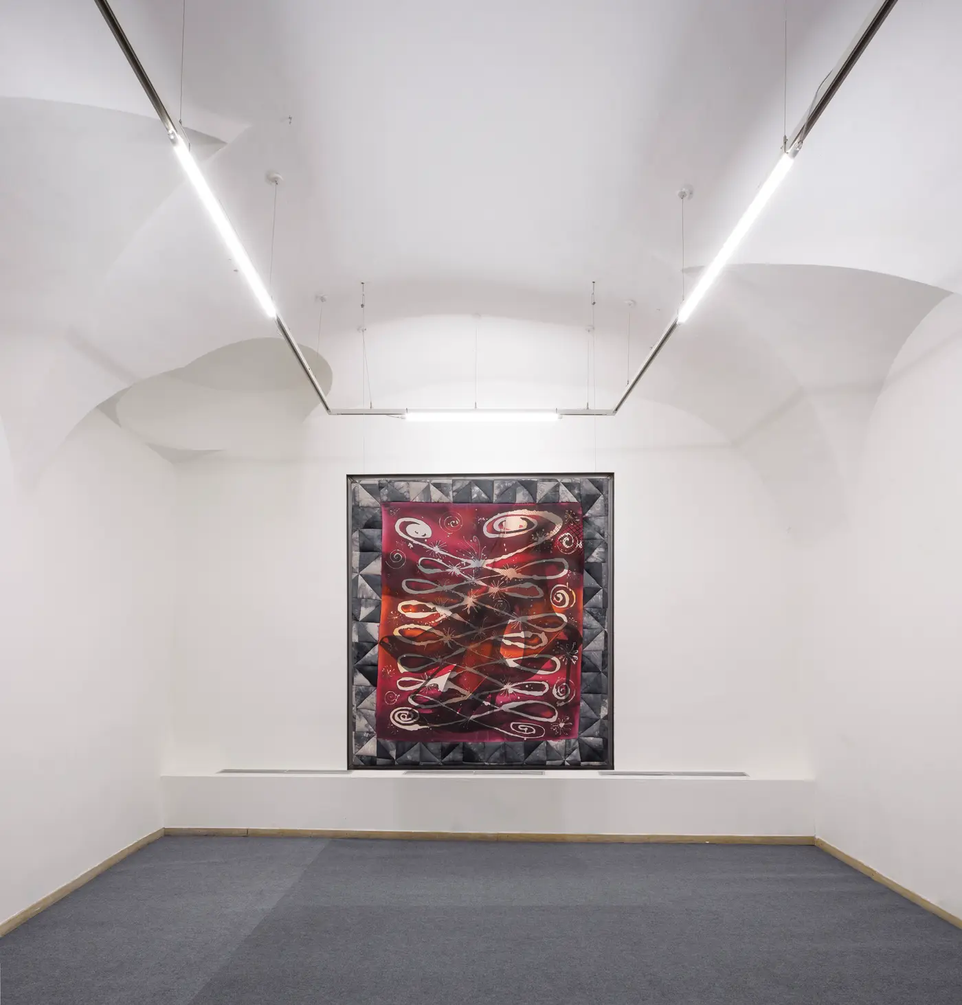 Installation view of a large abstract painting by Bety Krňanská, featuring swirling red and grey forms framed with geometric quilting motifs, shown at Galerie AMU in Prague