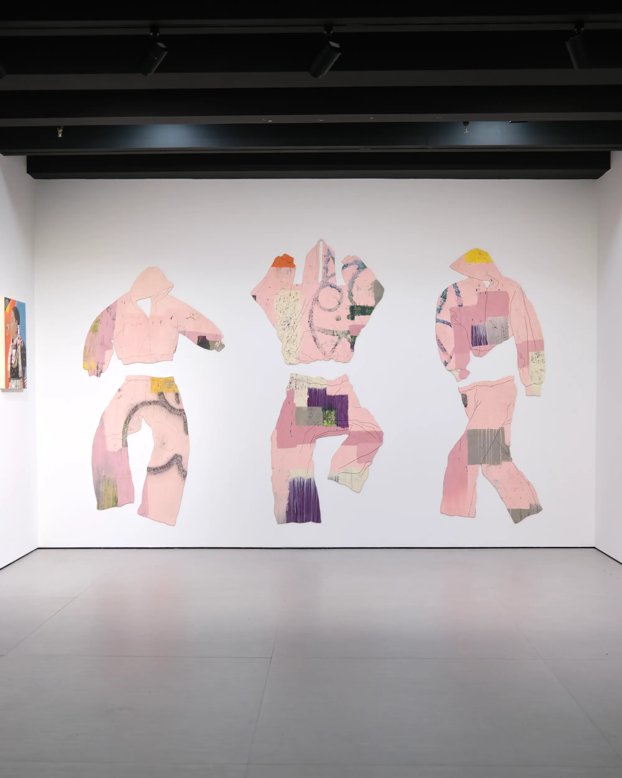 Three large cut-out clothing forms mounted on a white wall; painting behaving as sculpture.