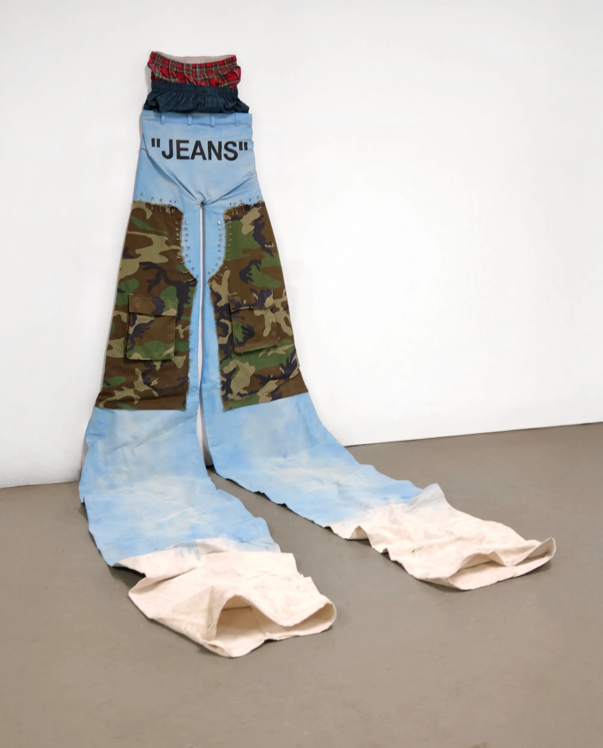 Oversized sagging jeans with camo pockets and sky-blue legs extending across the floor; streetwear as landscape.