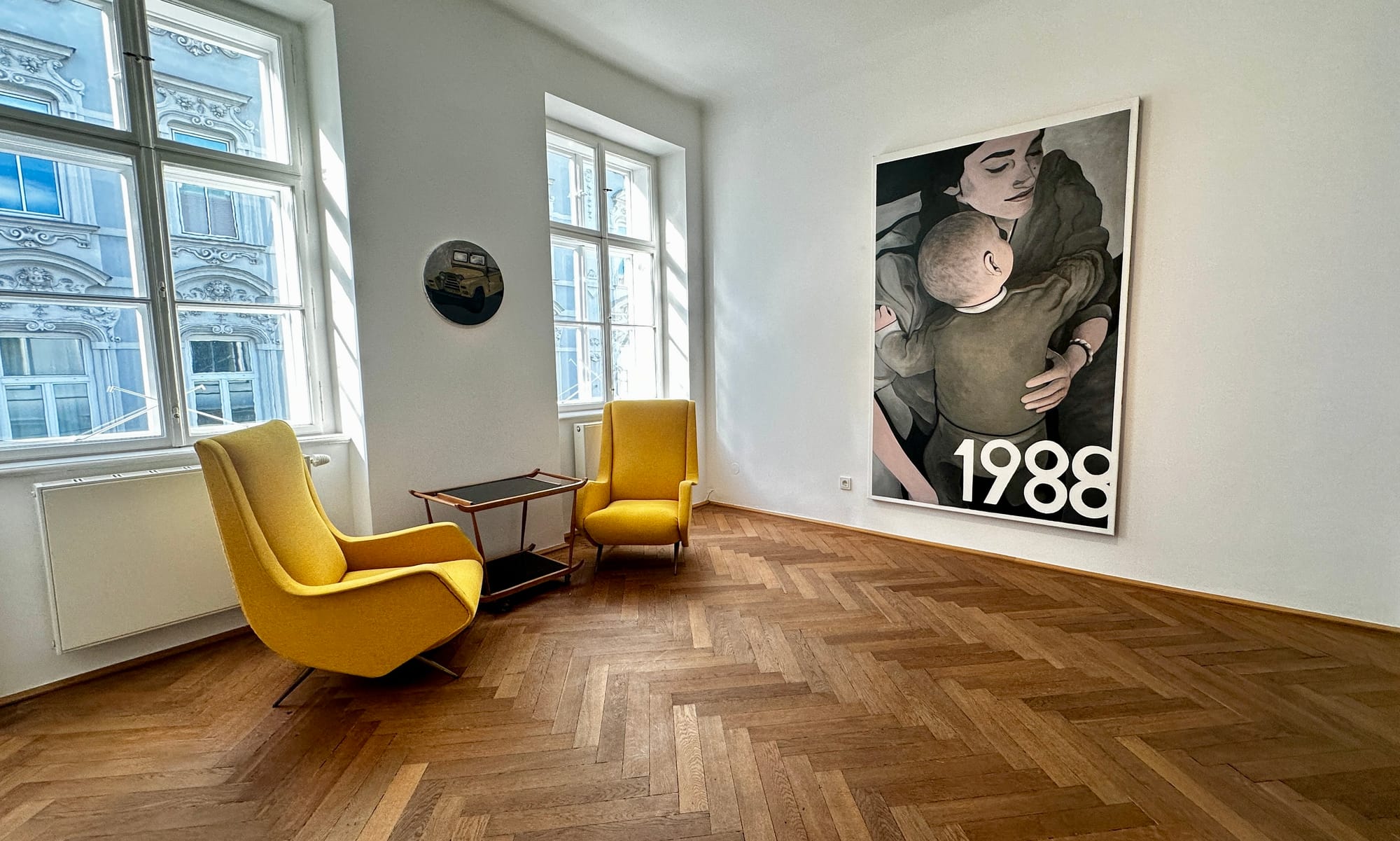 Room view at Klubhaus showing a small round Jeep painting and a large mother-and-child painting from “1996.”