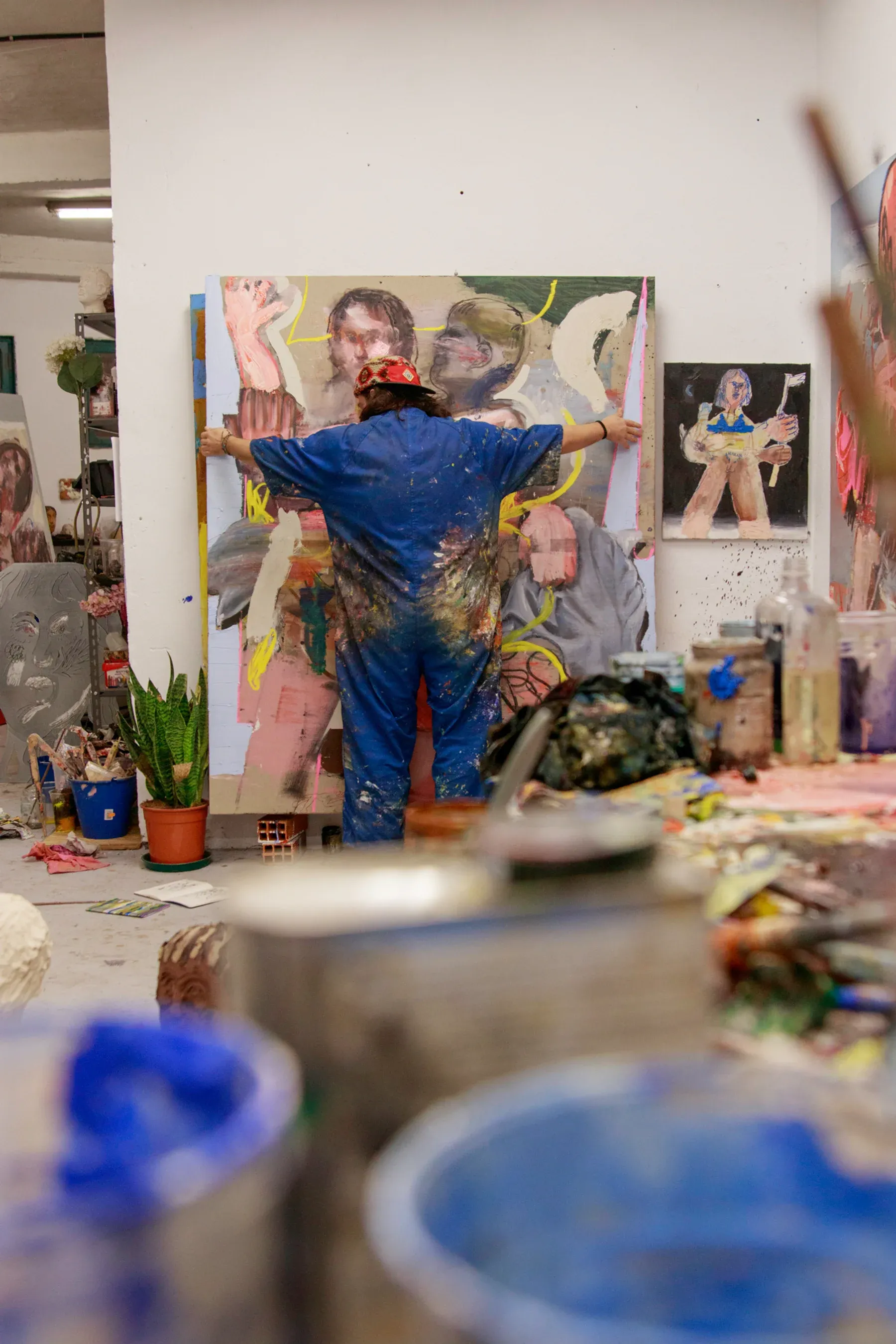 Manuel García Fernández in his studio wearing a paint-covered jumpsuit, stretching his arms across a large figurative canvas. Photo by Juan García-Mendoza.