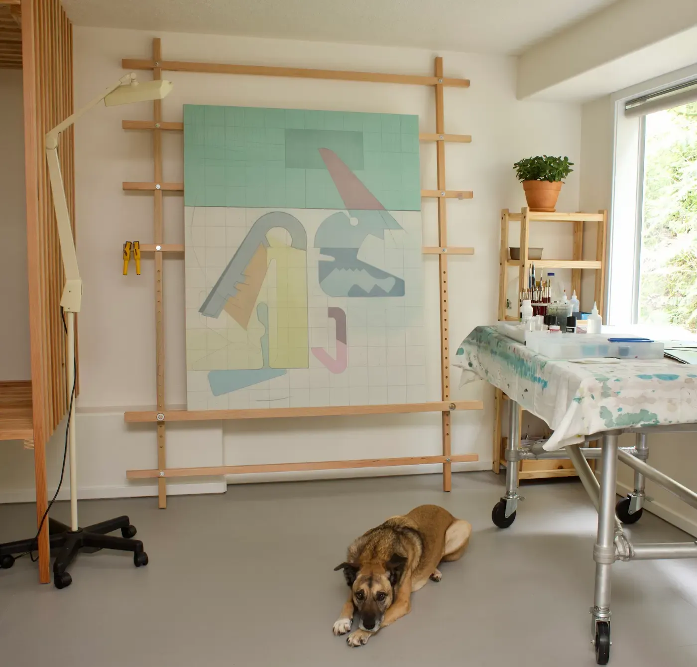 Dog Laika lying on the floor in Chris Cassimatis’s basement studio in 2023, surrounded by painting tables and a work in progress. Image Courtesy of the Artist.