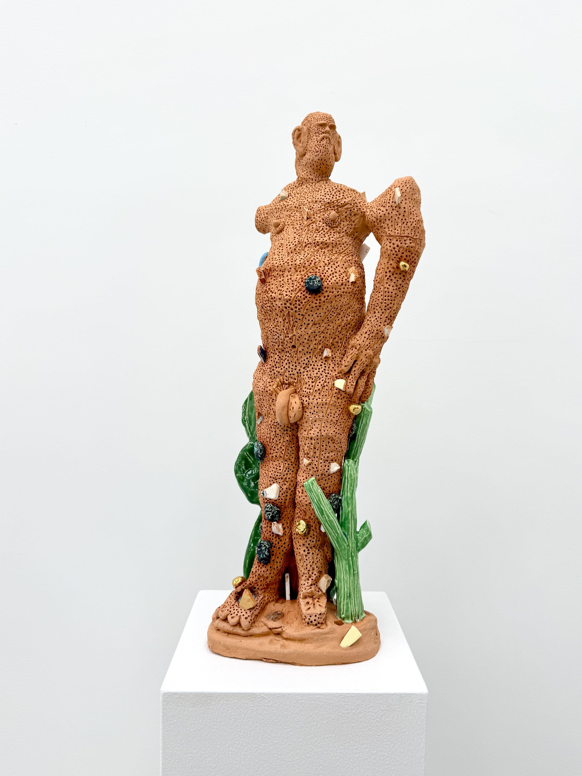 Terracotta sculpture by Glenn Barkley titled The Sculptor (2025), depicting a nude standing male figure embedded with colorful glazed elements and surrounded by green ceramic plants, shown on a white pedestal at HAGD Contemporary, Aalborg, Denmark