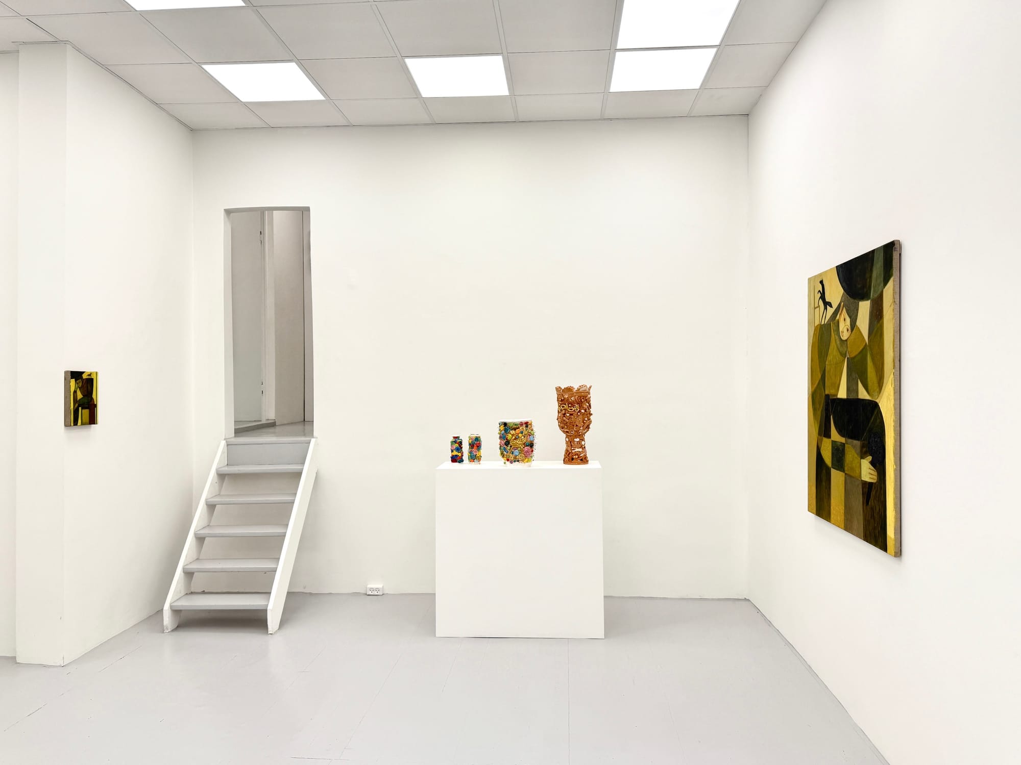 Installation view at HAGD Contemporary, Aalborg, Denmark, showing a terracotta sculpture by Glenn Barkley centered between two ochre-toned figurative paintings by Bob Geerts on white walls beside a narrow stairway.