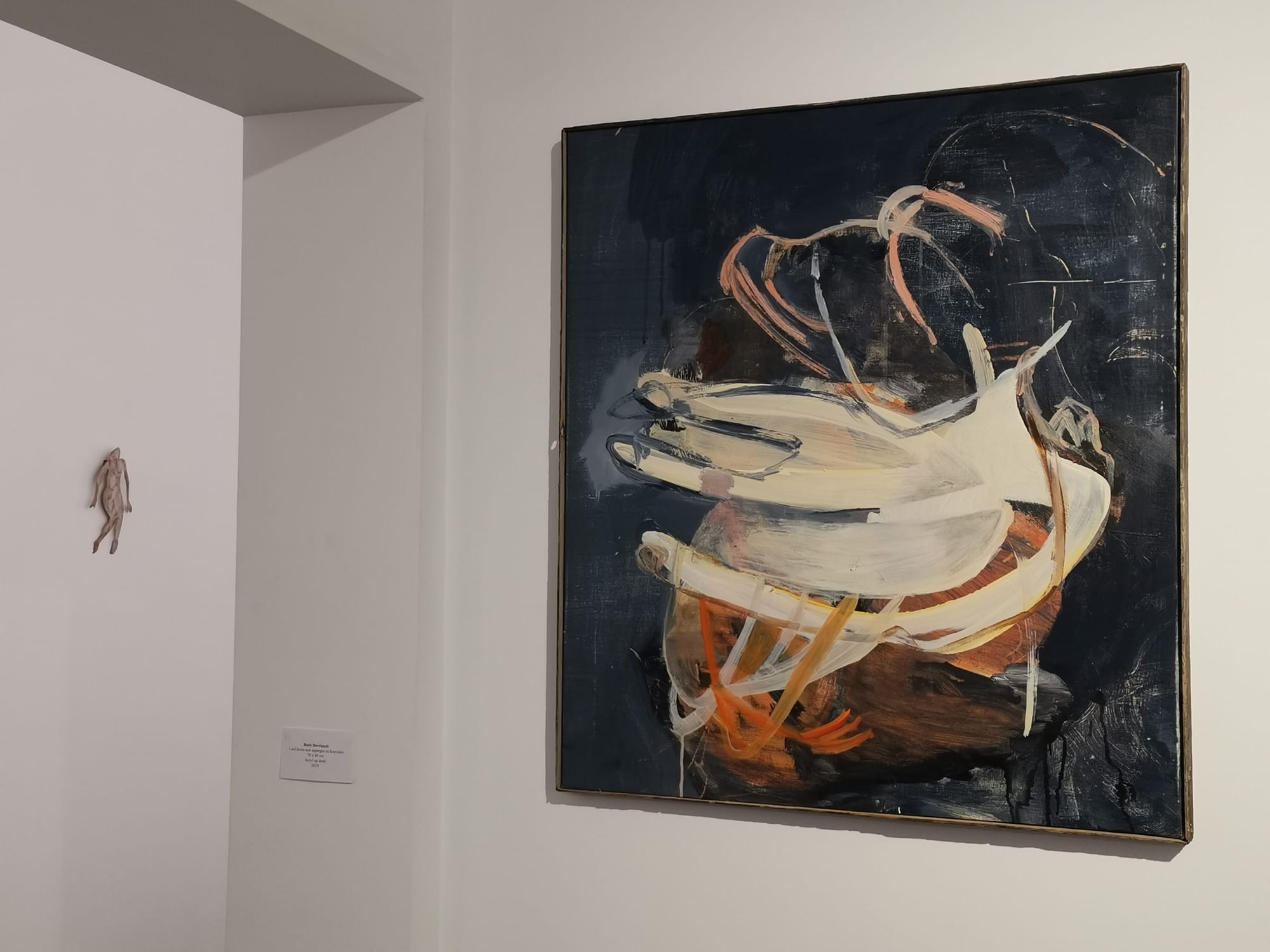 Ruth Devriendt’s 2019 painting Loud life with asparagus and headmeat, acrylic on canvas, shown mounted on a white gallery wall near a small sculptural element. Image courtesy of the artist.