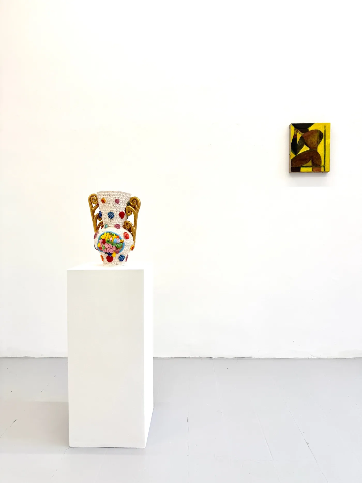 Installation view at HAGD Contemporary, Aalborg, Denmark, showing a colorful earthenware vase by Glenn Barkley on a white pedestal beside a small ochre-toned geometric portrait painting by Bob Geerts on a white wall.