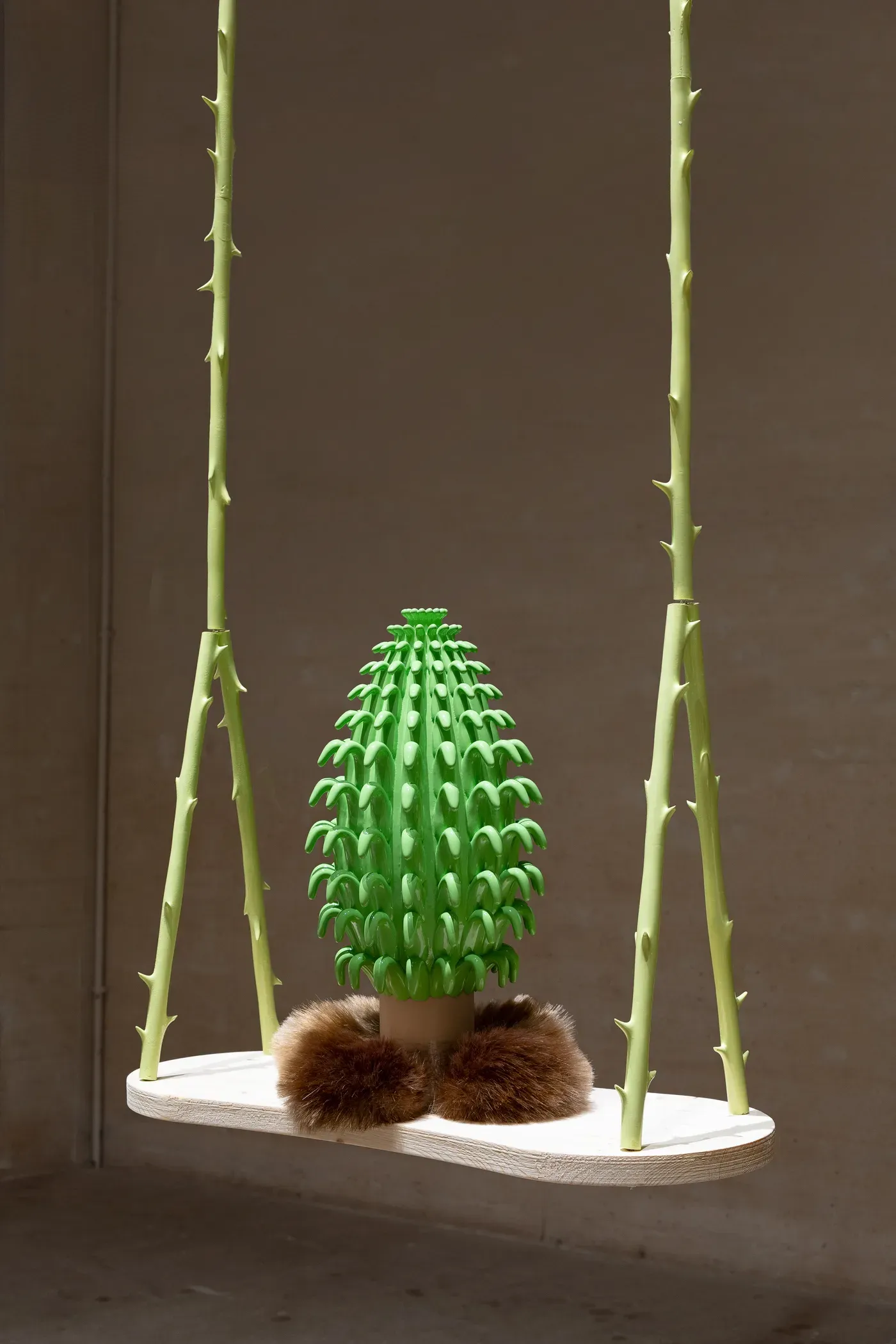 new artist working with ceramic in installation - A suspended installation by Grip Face showing a bright green ceramic object with layered spikes, resting on a wooden swing held by pale thorn-like rods, displayed in a neutral gallery space at the Miró Foundation.