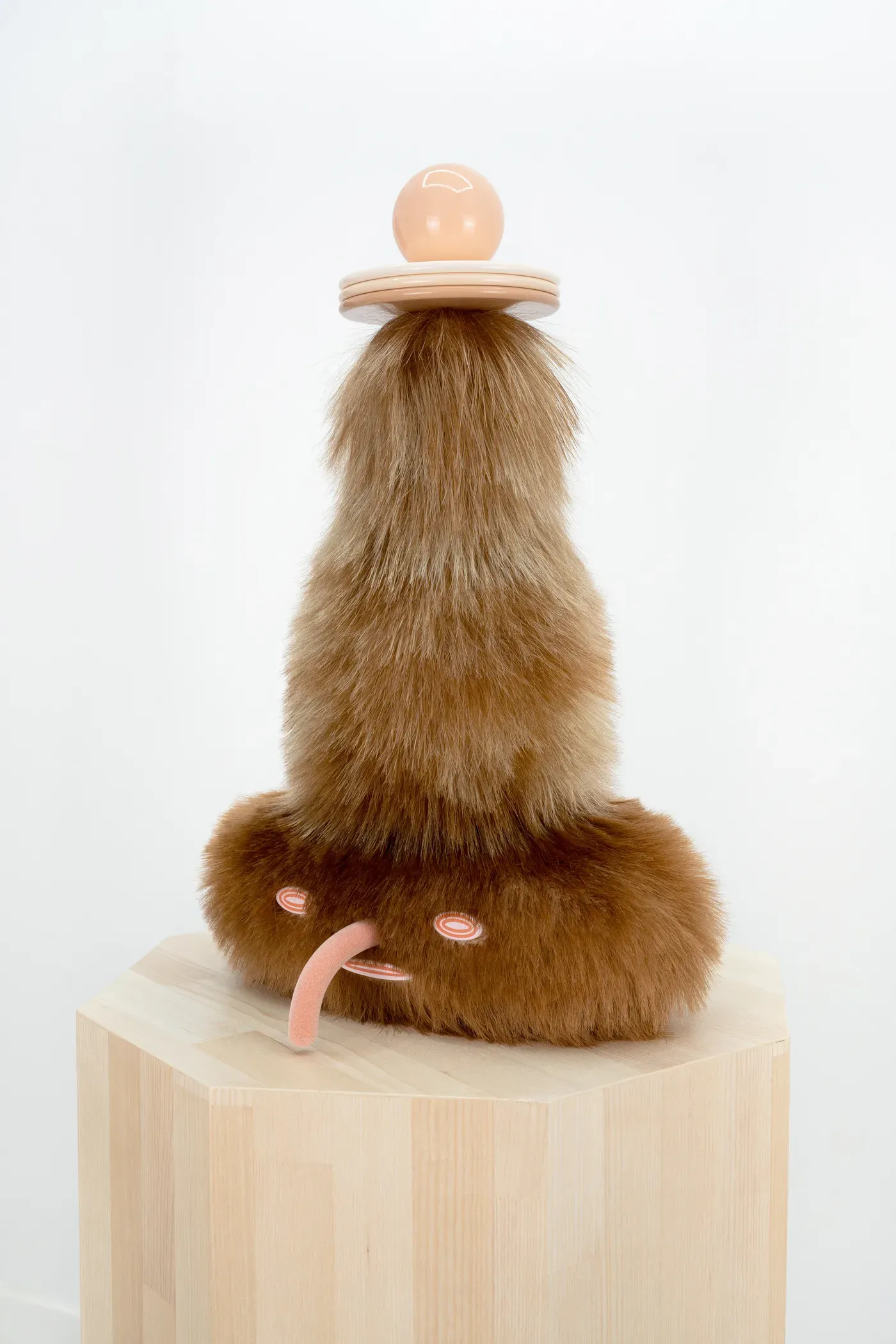 Close-up of the sculpture De máscara a placebo insomne by Grip Face. A furry, brown form with synthetic hair, a small protruding tongue-like element, and circular eyes sits on a wooden plinth. Made of resin, silicone, aluminium, and enamel. Exhibited at @feriaarco with @galeriampa