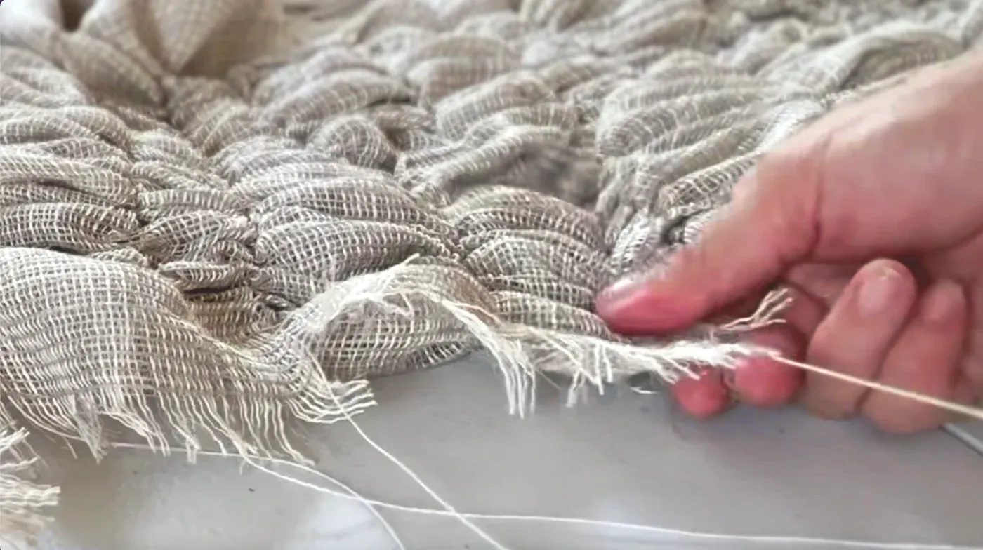 Yali Romagoza, Landscapes of Belonging (2025), close-up still showing the artist’s hand pulling individual linen threads during the making process of her textile sculpture.