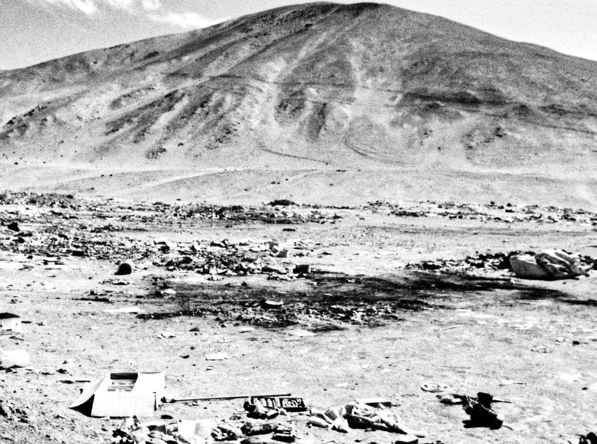 Black-and-white desert landscape photograph from Emergent Phenomenon by Nadine Karl, showing rocky ground and sparse objects in an open landscape.