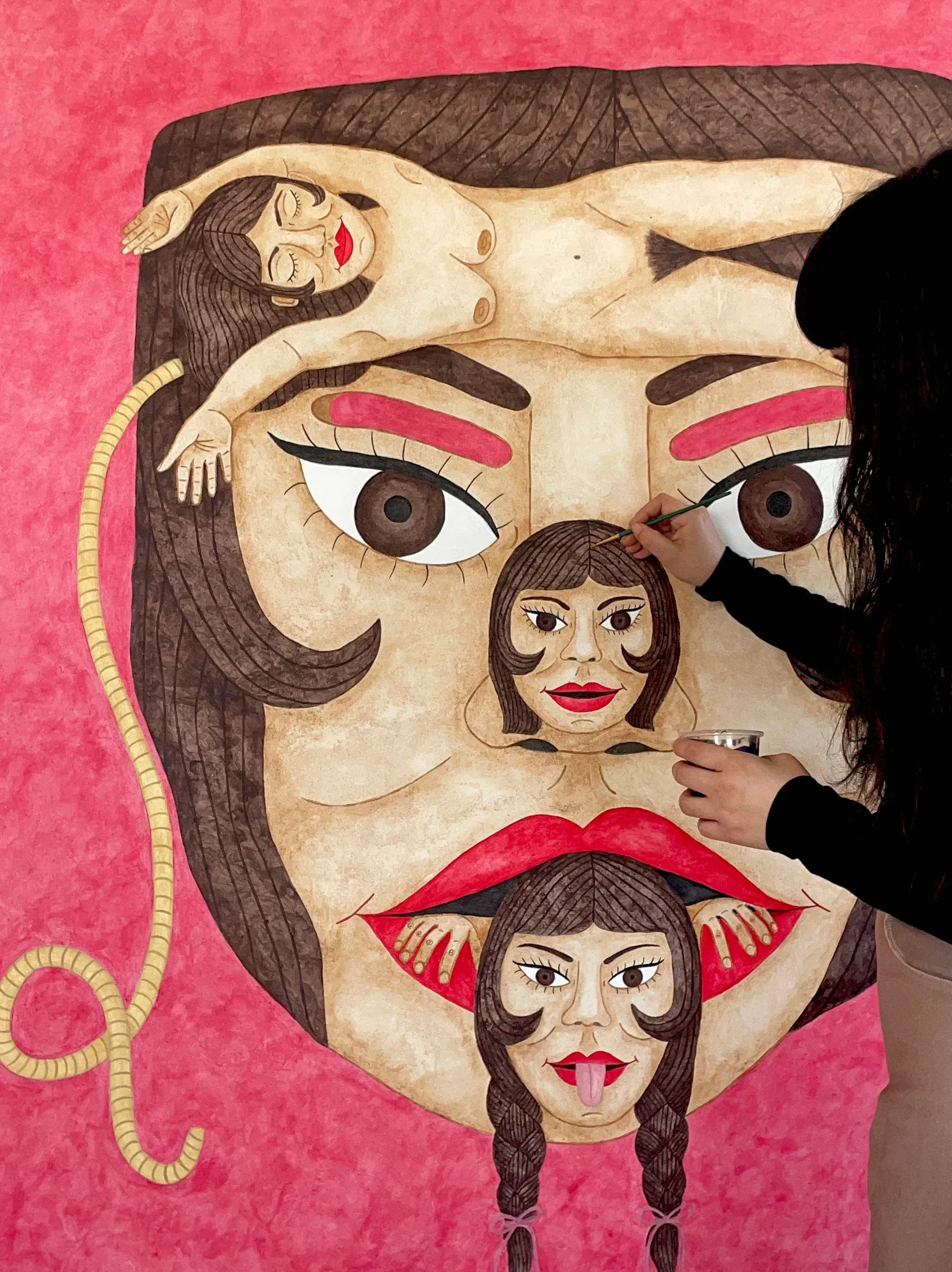 Artist painting a large pink background portrait composed of nested faces, with one central large face containing smaller faces within.