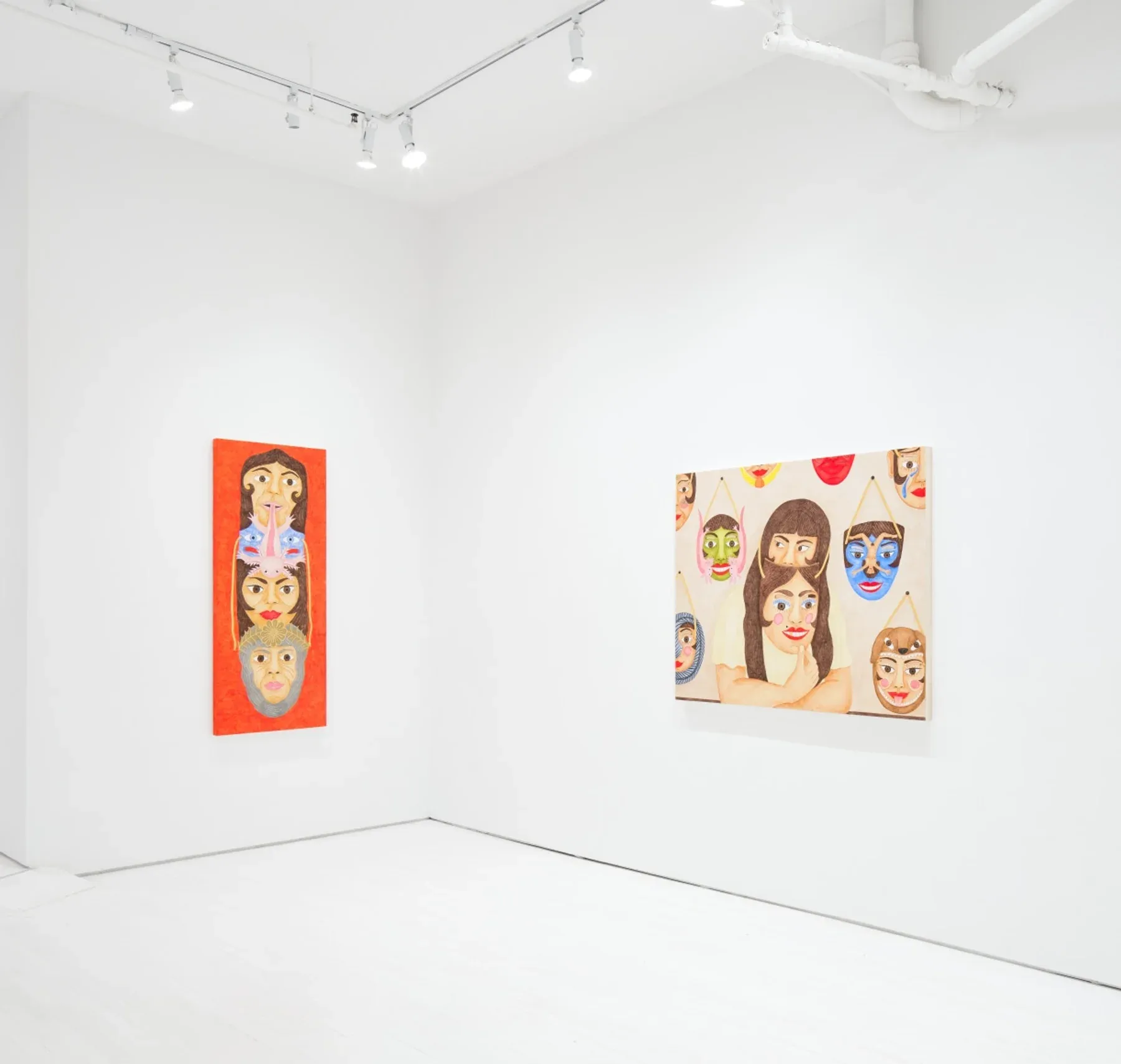White gallery with two paintings: one tall red piece featuring stacked masked faces, and one horizontal canvas with multiple mask-like portraits.