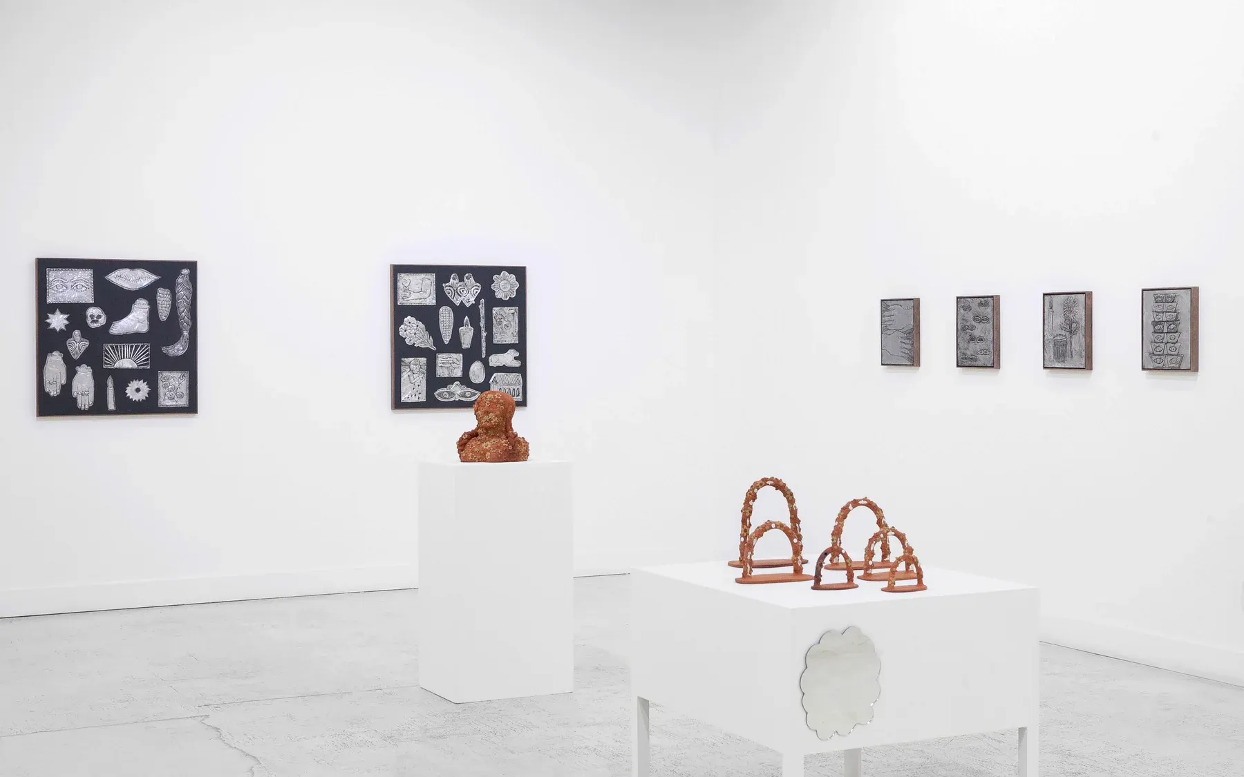 Alt text: Terracotta sculptures and framed monochrome drawings arranged across a bright gallery corner.