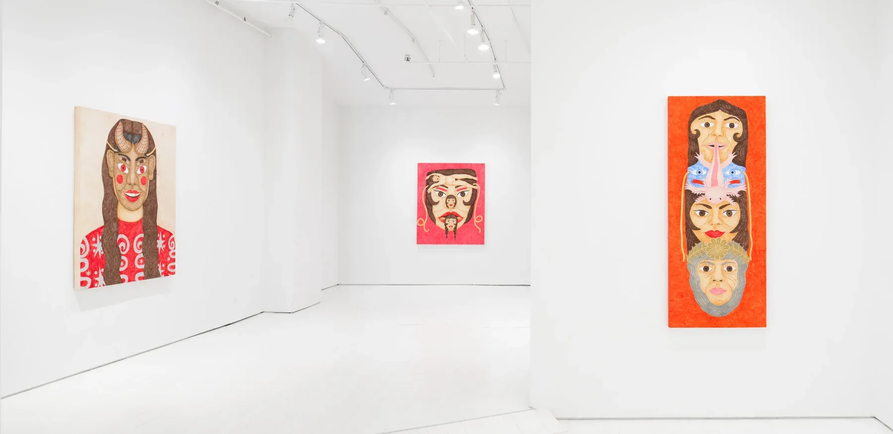 White gallery with two paintings: one tall red piece featuring stacked masked faces, and one horizontal canvas with multiple mask-like portraits.
