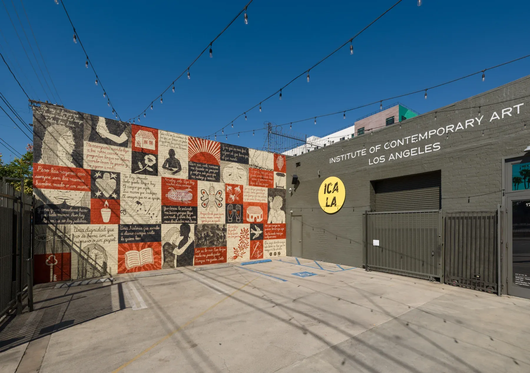 Angled view of the full ICA LA courtyard mural with red, cream, and black illustrated squares and string lights above.