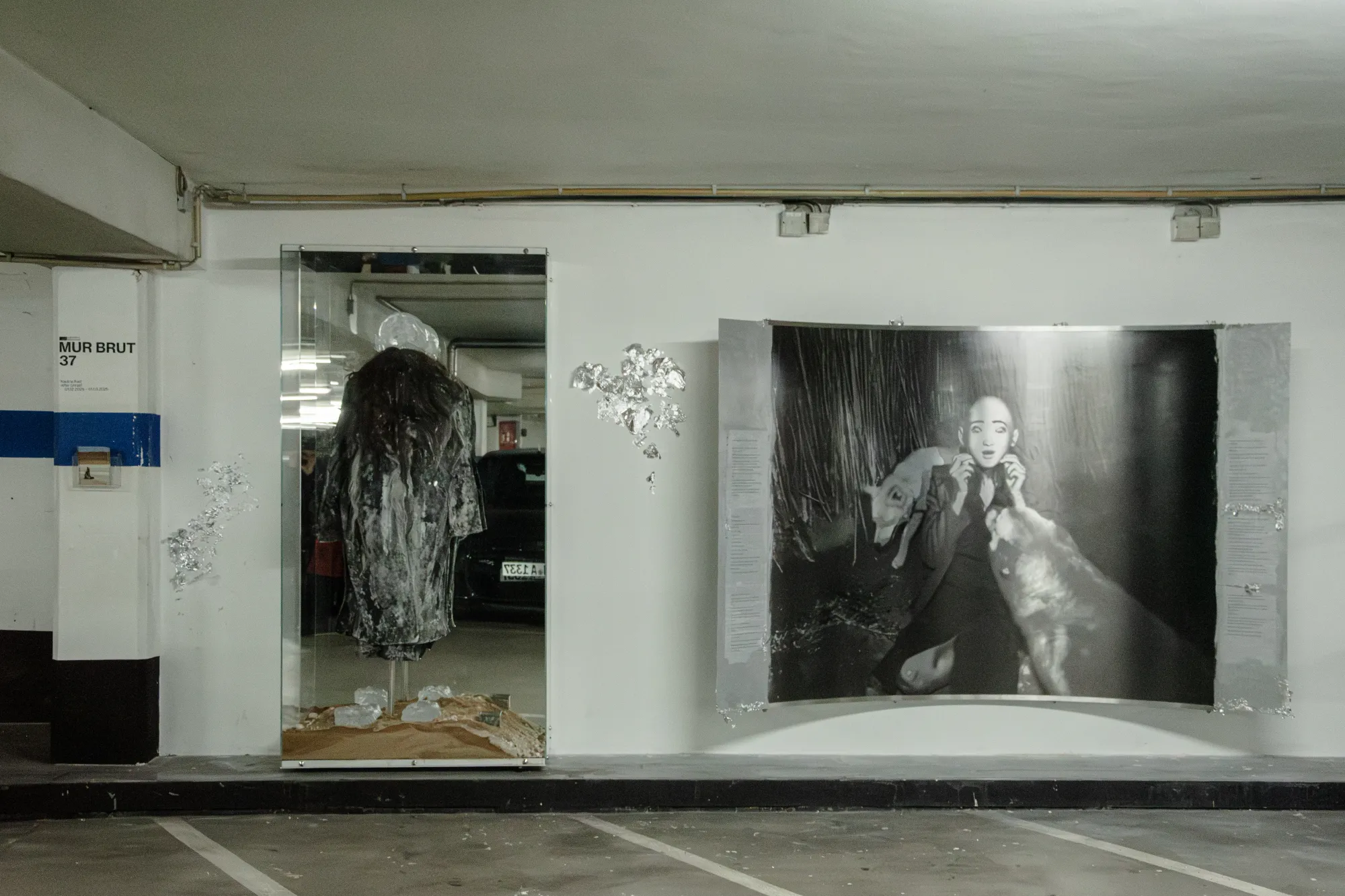 Installation view of After Unrast by Nadine Karl at Kunsthalle DĂĽsseldorf, showing a glass display with sculptural elements and a large black-and-white photographic work mounted on the wall.
