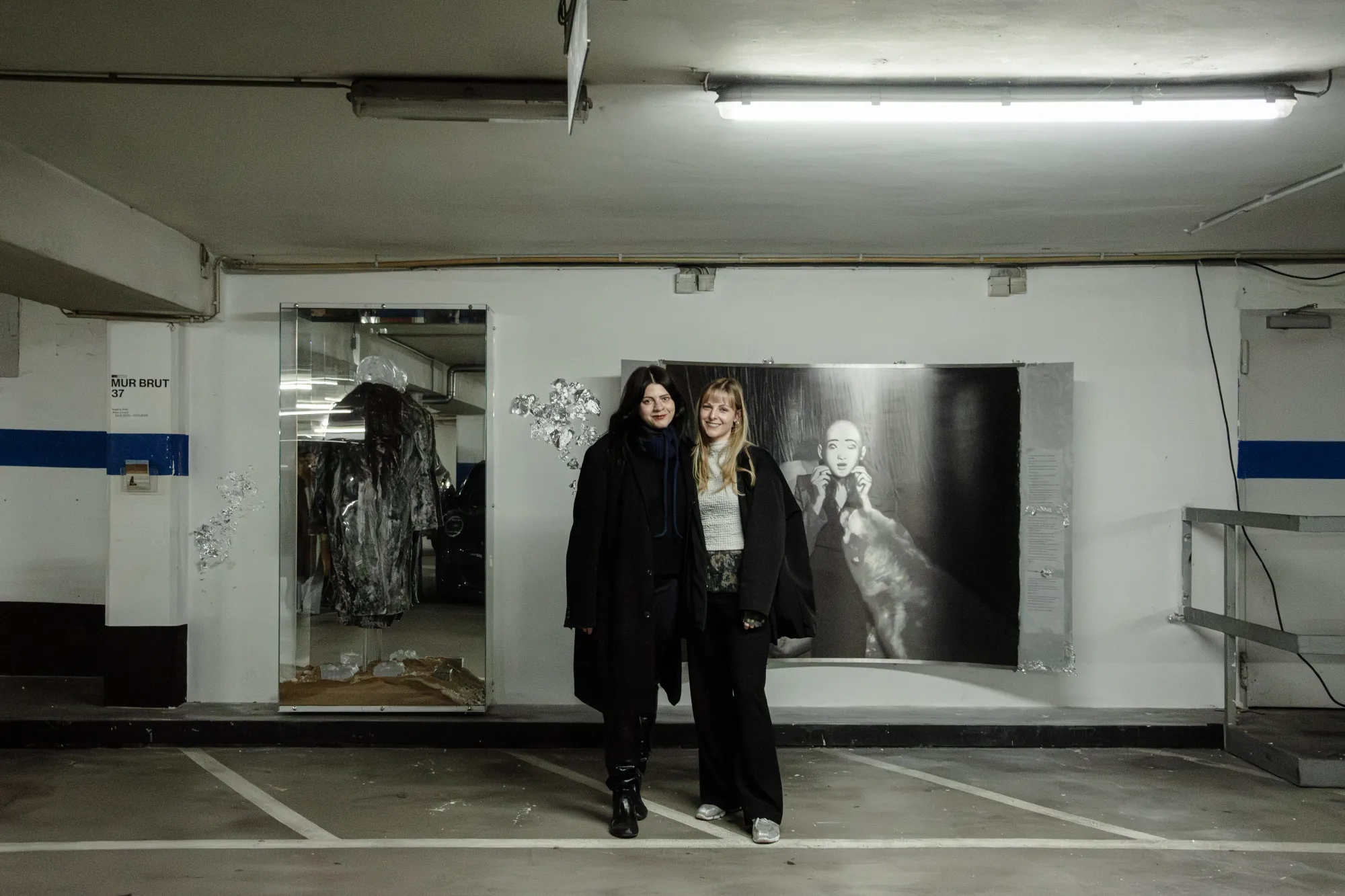 Installation view of After Unrast by Nadine Karl at Kunsthalle DĂĽsseldorf, showing the artist on the left, standing in front of the installation with sculptural and photographic works visible in the background.