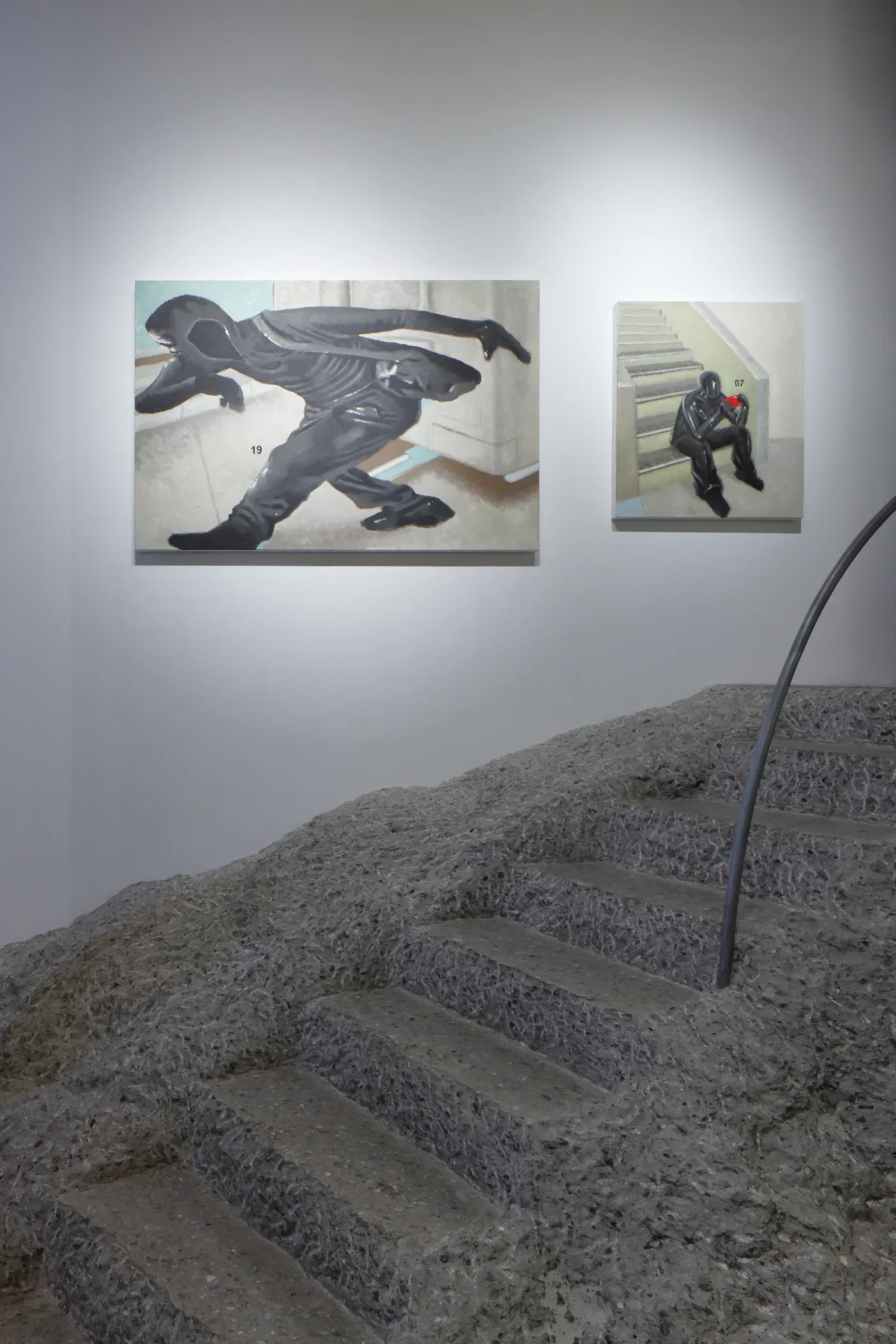 Exhibition view showing two paintings of black clad figures on a gallery wall above textured sculptural stairs.