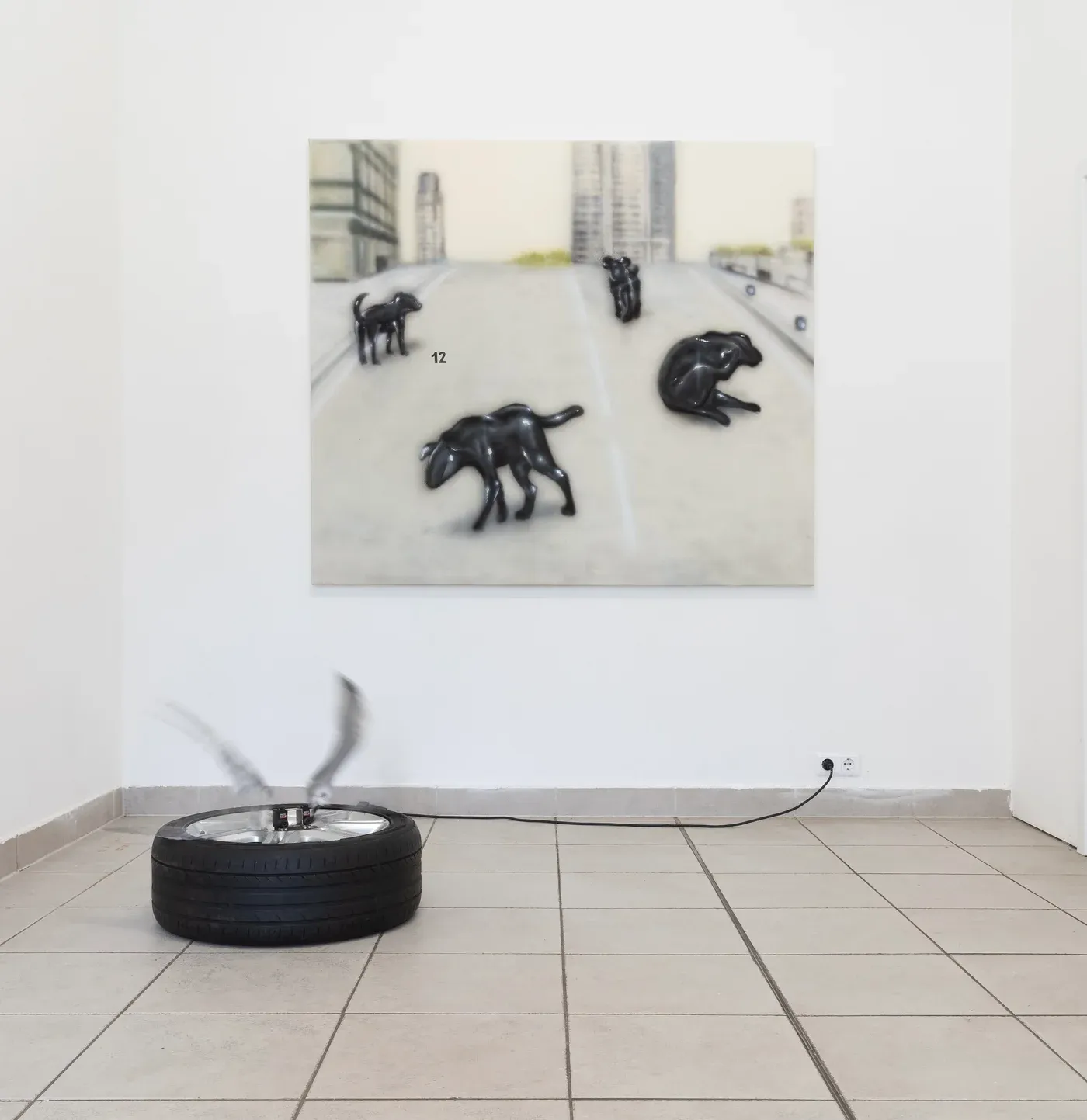 Yutaro Inagaki, Gallery installation showing a painting of multiple black dog forms in an empty city road, accompanied by a spinning tire sculpture on the floor.