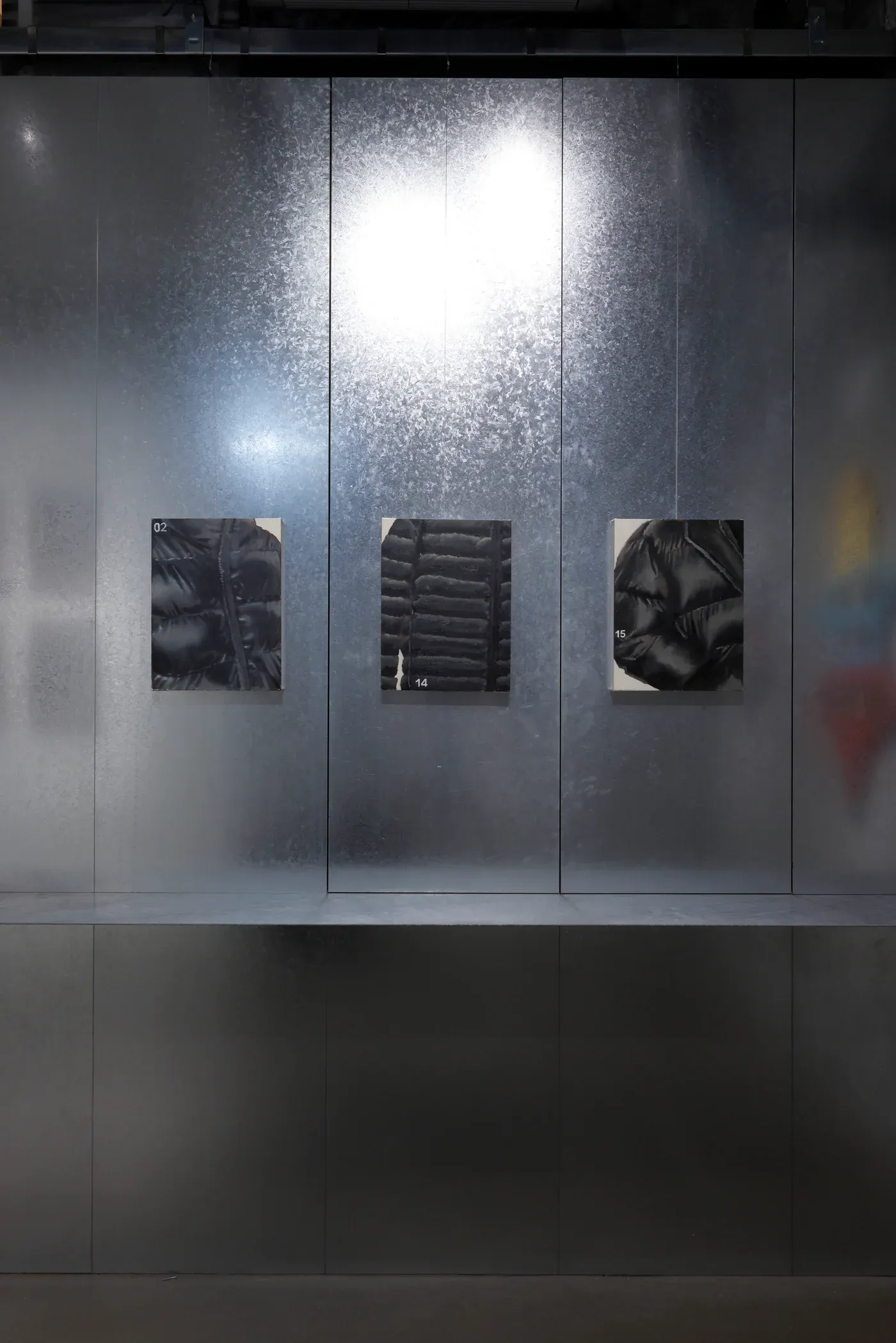 Three close cropped puffer jacket studies displayed on a metallic gallery wall, each painting focusing on glossy padded surfaces.