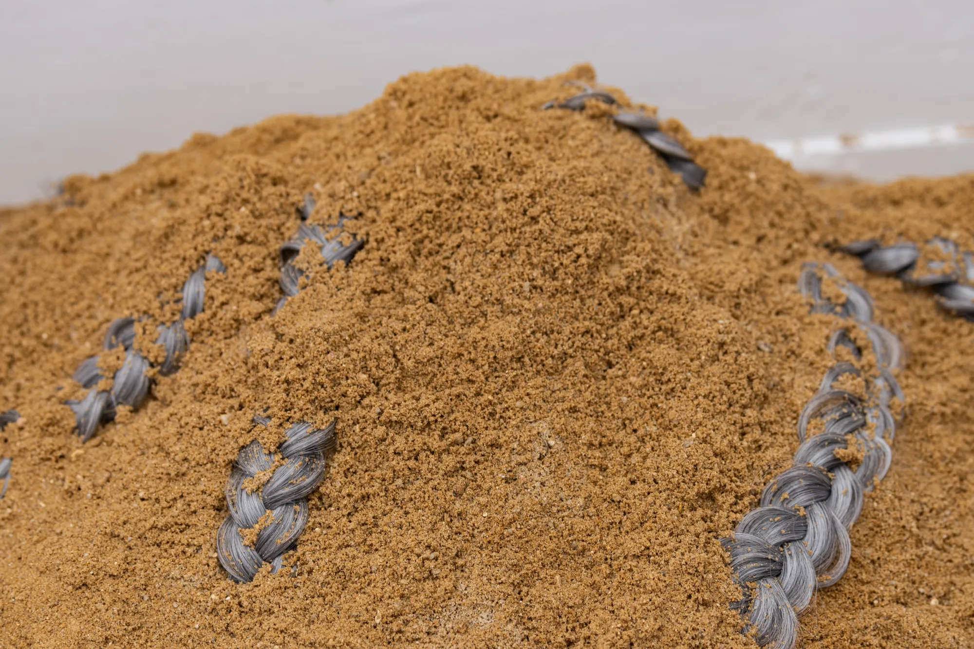 Close-up view of Epiphenomenon by Nadine Karl, focusing on a sand mound with braided material emerging from the surface.