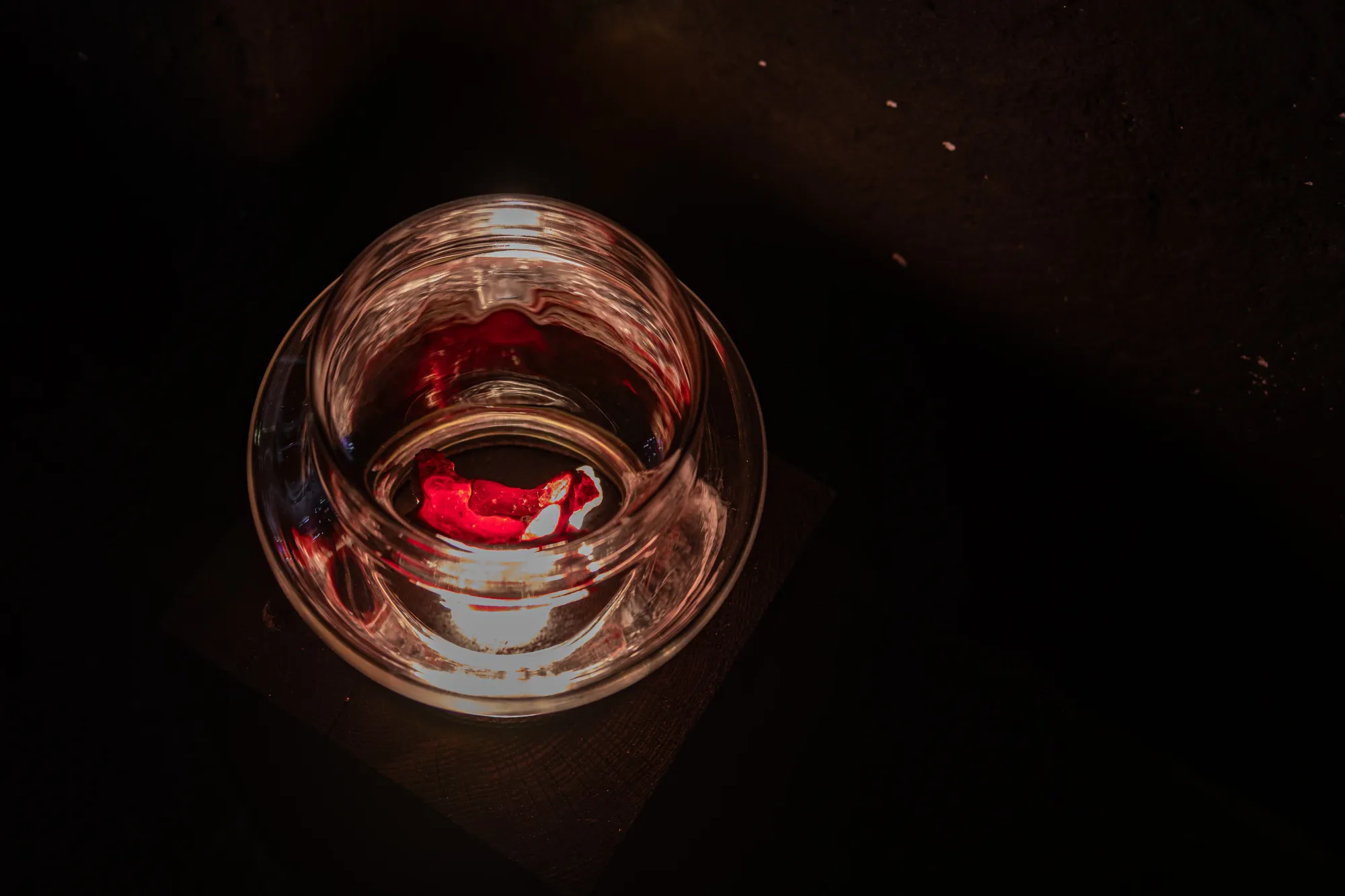 Installation detail from Epiphenomenon by Nadine Karl, showing a glass vessel containing a red sculptural element, illuminated against a dark background.