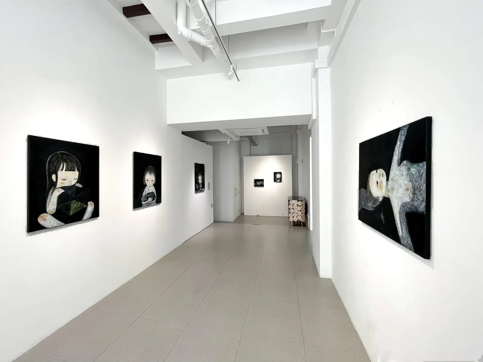 Installation view of paintings by Ruo-Hsin Wu displayed in a white gallery space at Cuturi Gallery, featuring pale figurative works set against dark backgrounds.