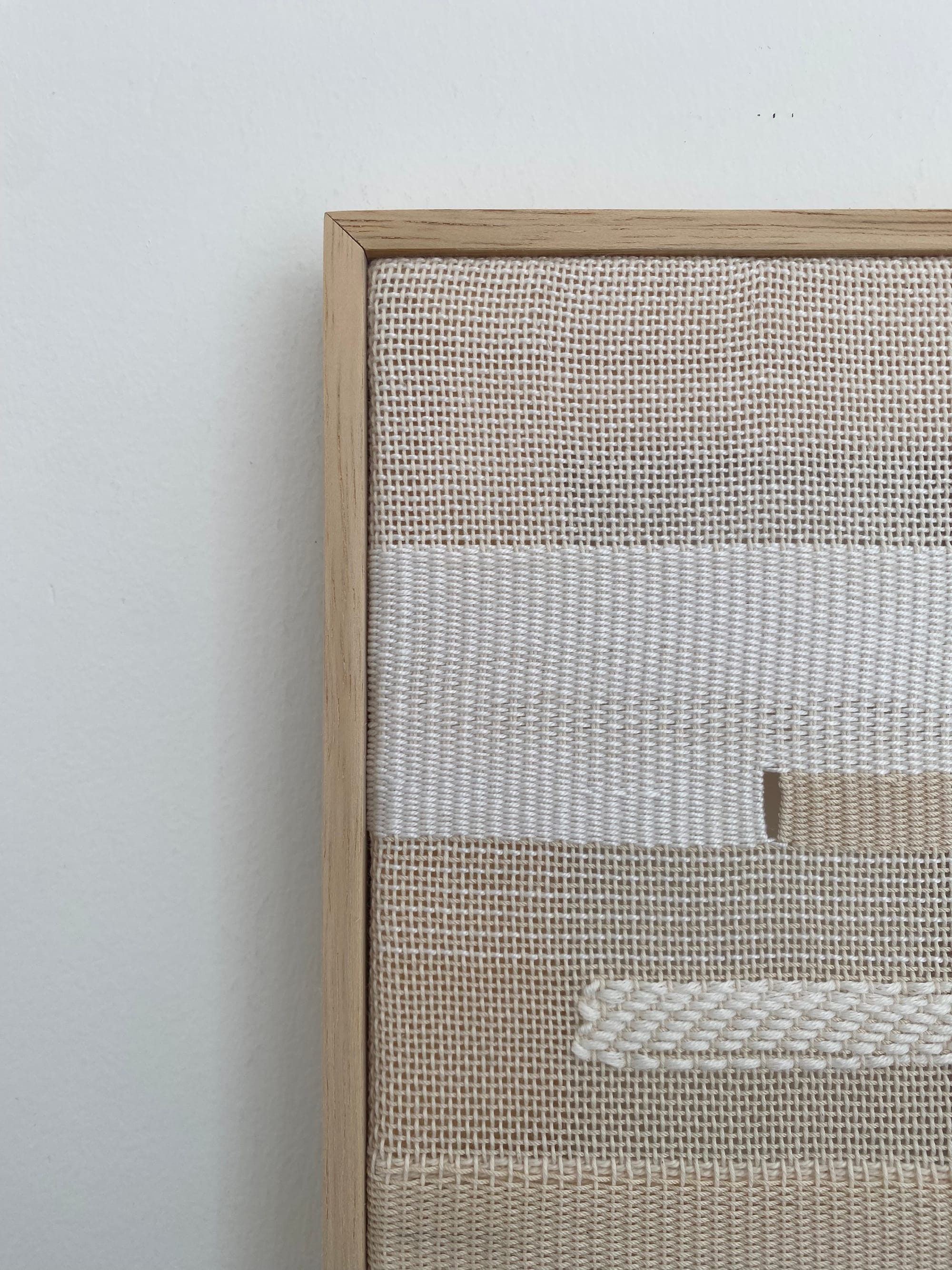 Detail of a hand woven textile surface showing layered threads and shifts in texture within a wooden frame, emphasizing material structure and weave pattern.