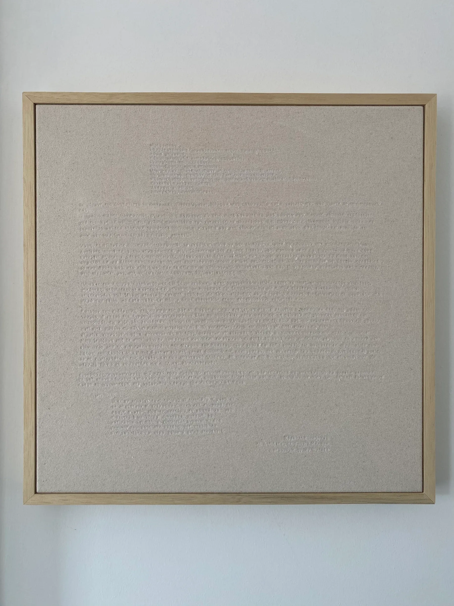A framed textile work made of canvas with subtle stitched text across a pale surface, emphasizing quiet texture and restrained material presence.