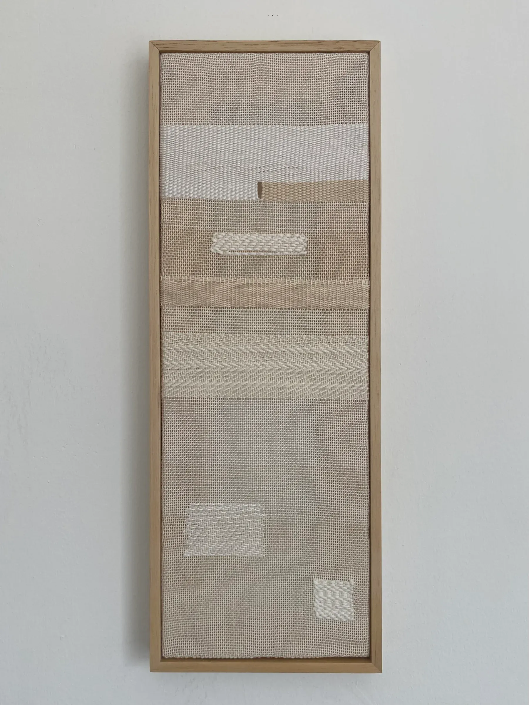 A vertically oriented framed textile work composed of hand woven thread on canvas, arranged in horizontal bands with subtle variations in weave density and tone.