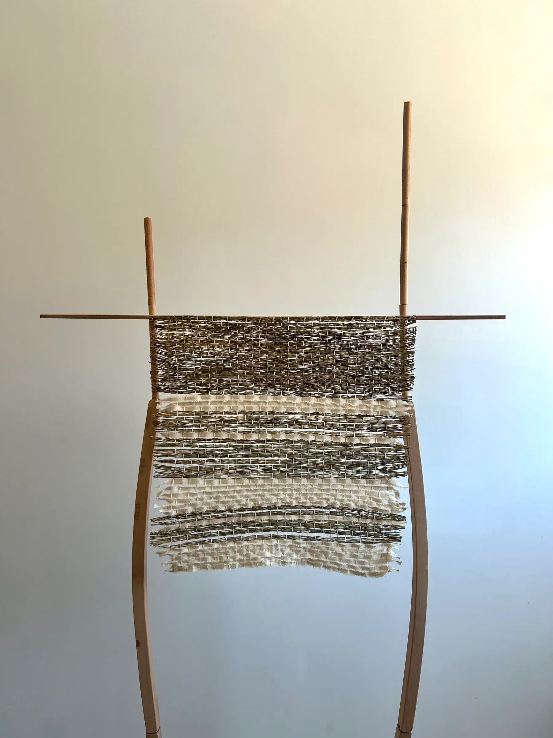 A tall wooden frame holding woven straw and canvas strips with varied density that creates soft changes in light and texture.