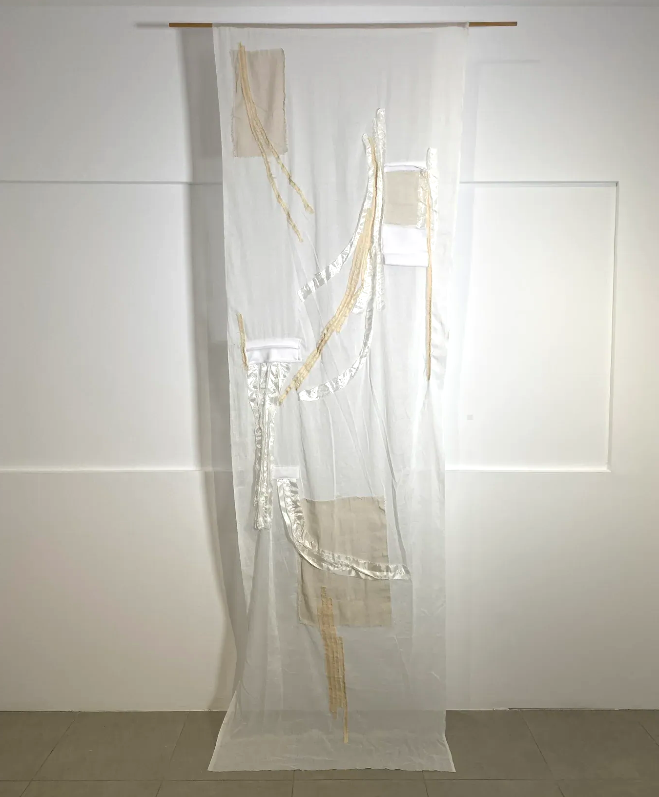 A suspended textile work made of translucent cheesecloth layered with stitched canvas, polyester and linen elements that respond softly to light.