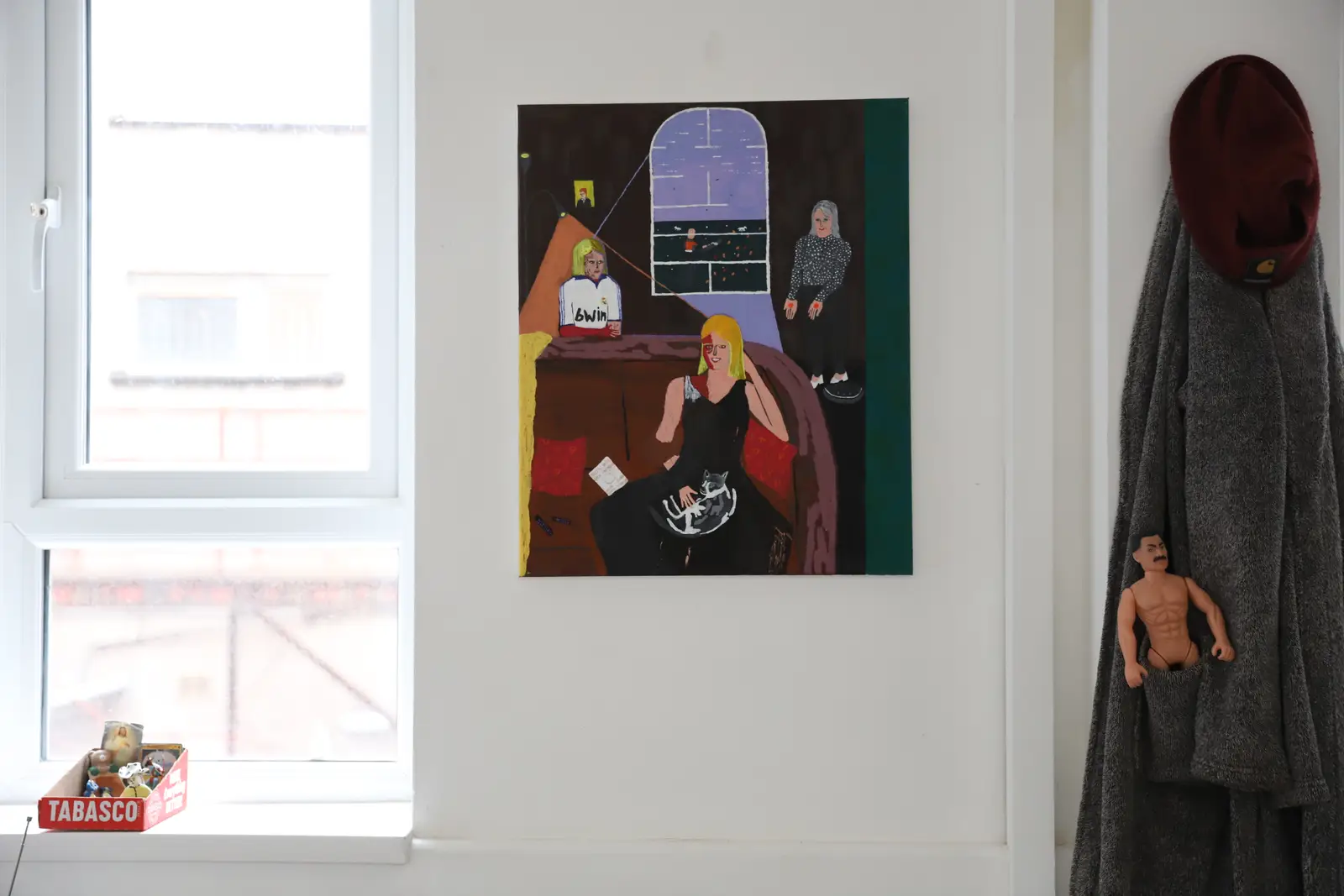 Paes painting displayed on a white wall near a window, with small objects placed below as part of the installation.