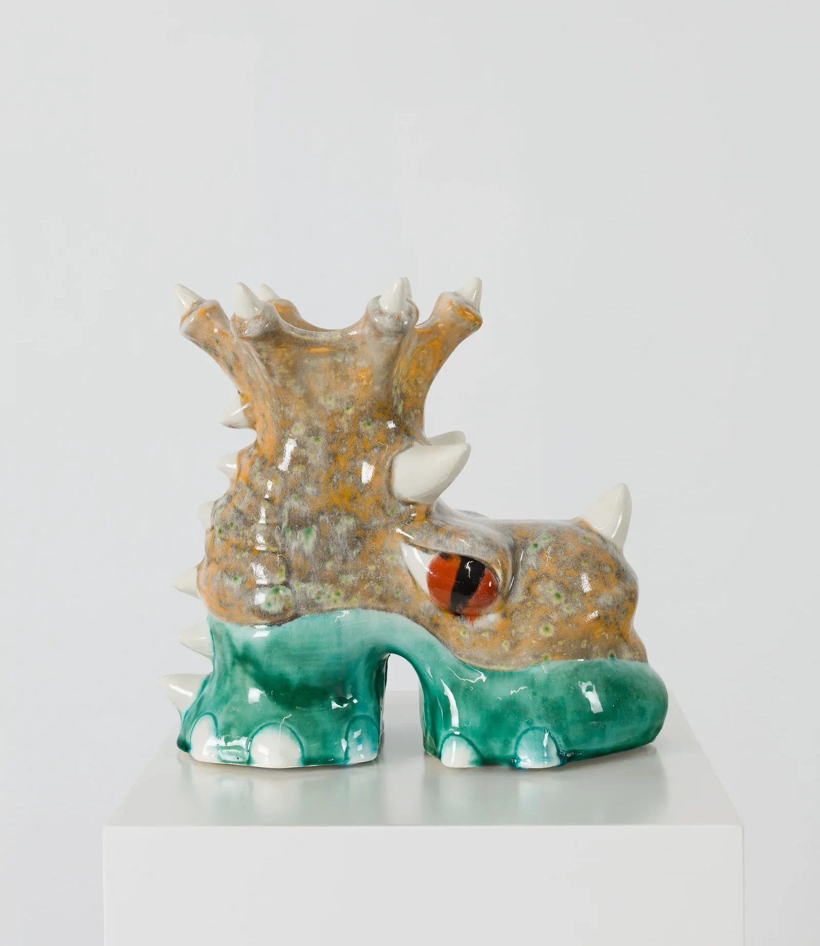 Ceramic sculpture by Fátima de Juan depicting a horned, creature-like form with glossy glazed surface, shown on a white plinth in an exhibition setting at Untitled Miami.