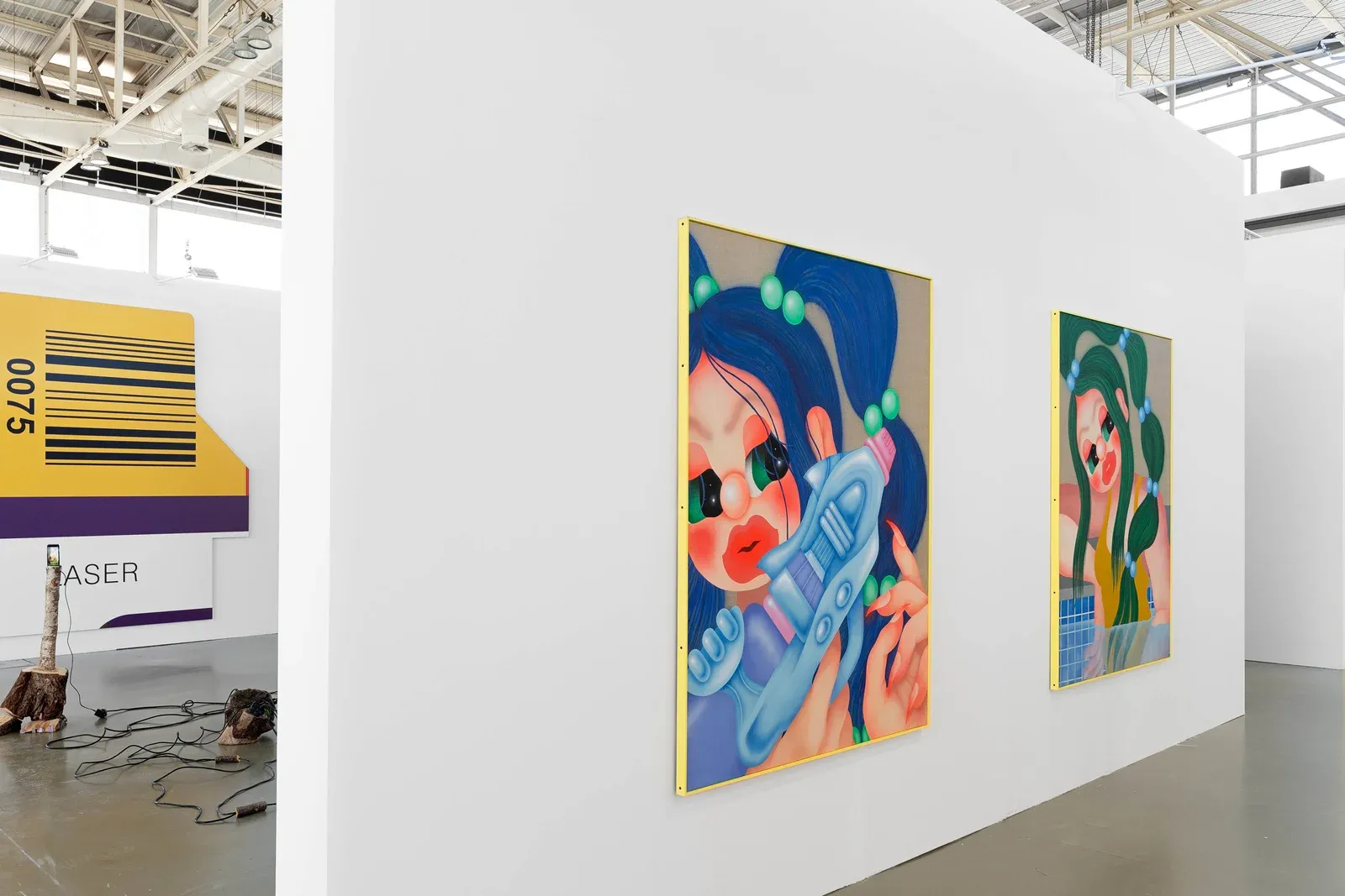 Installation view of Fátima de Juan’s paintings at CAN Ibiza, featuring colorful figurative works with stylized faces and toy-like objects displayed along a white exhibition wall.