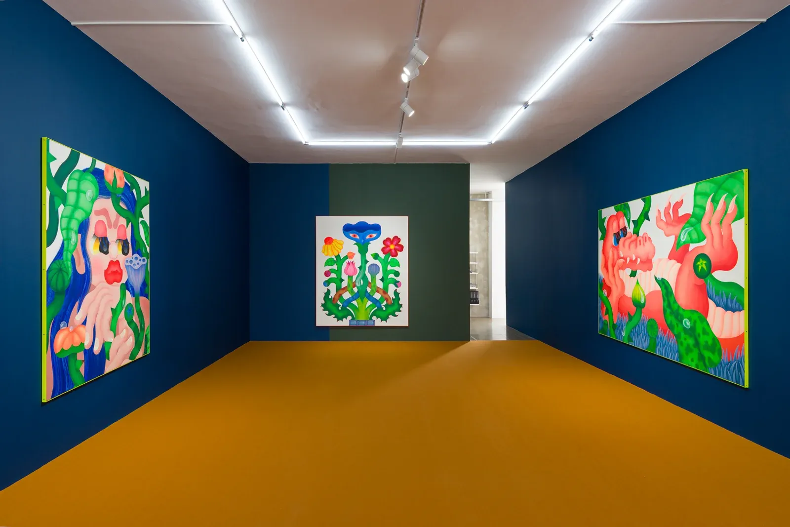 Wide installation view of a gallery space with brightly colored figurative paintings installed on deep blue walls and a contrasting floor.