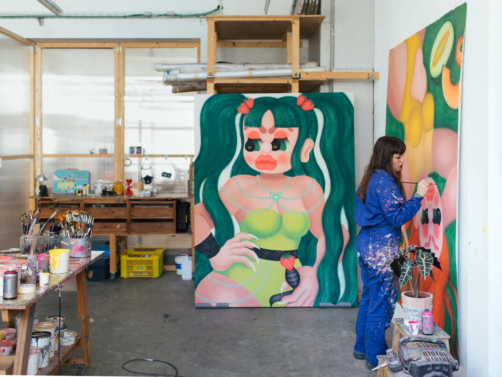 Fátima de Juan, Artist painting a large-scale figurative canvas in her studio, showing a stylized female figure and a working environment with brushes and paint containers.