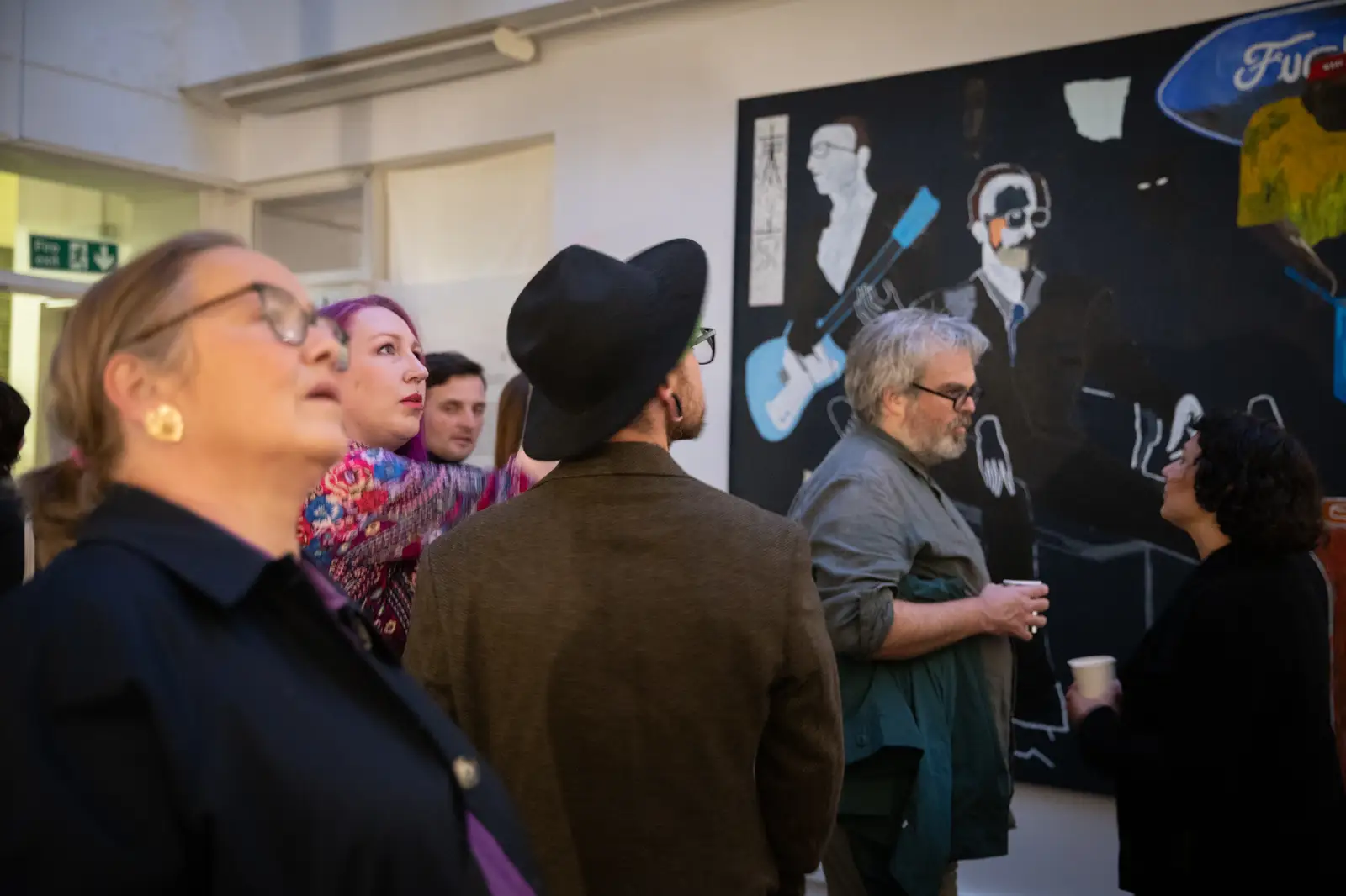 Visitors viewing Paes’ large-scale painting during the exhibition Faces I See When I Go to Sleep, showing figures inside a flattened bedroom interior