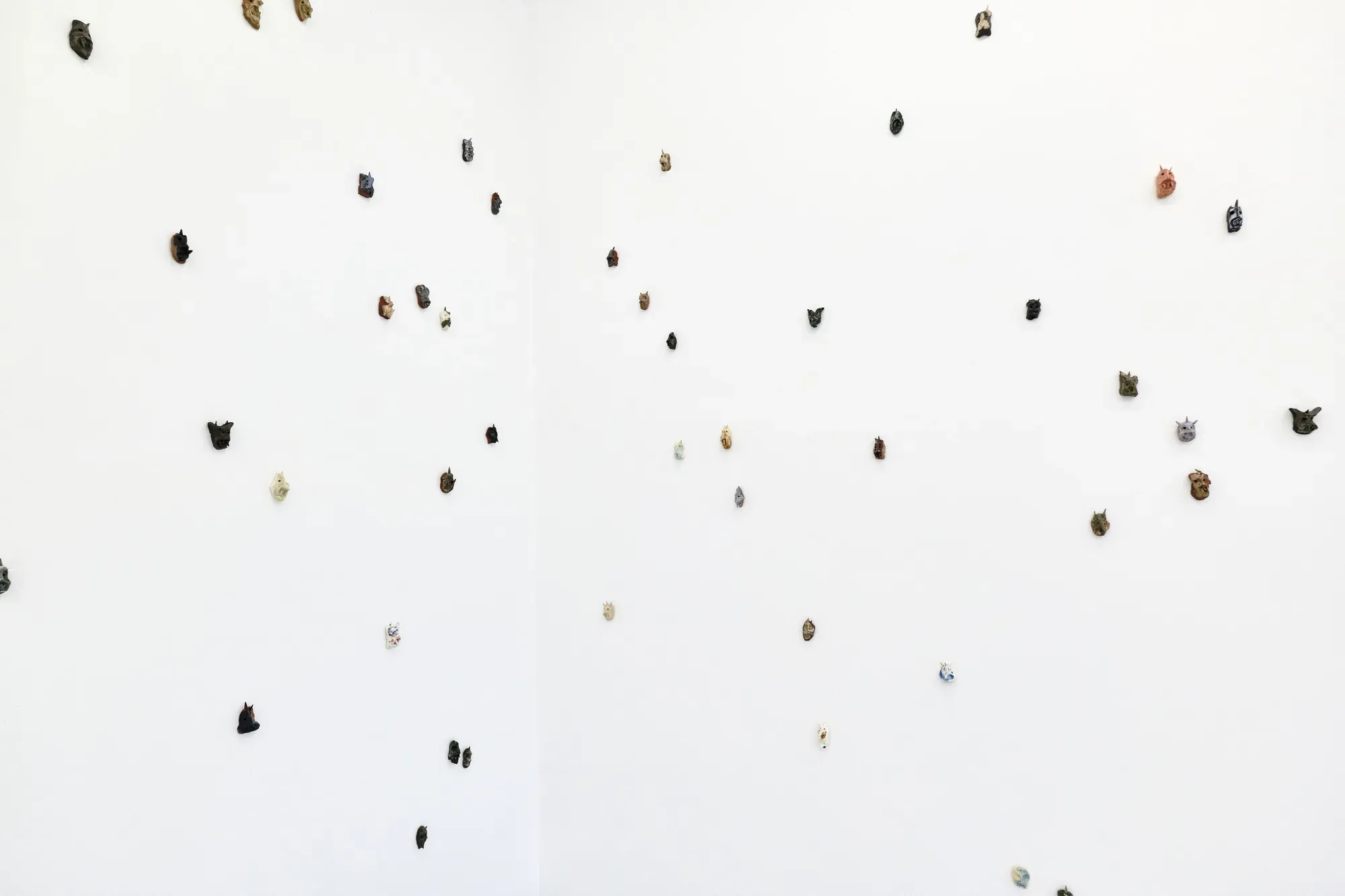 Installation detail of Mother of Many by Michael Kærgaard at HAGD Contemporary, Aalborg, showing small wall-mounted ceramic figures spaced across a white gallery wall