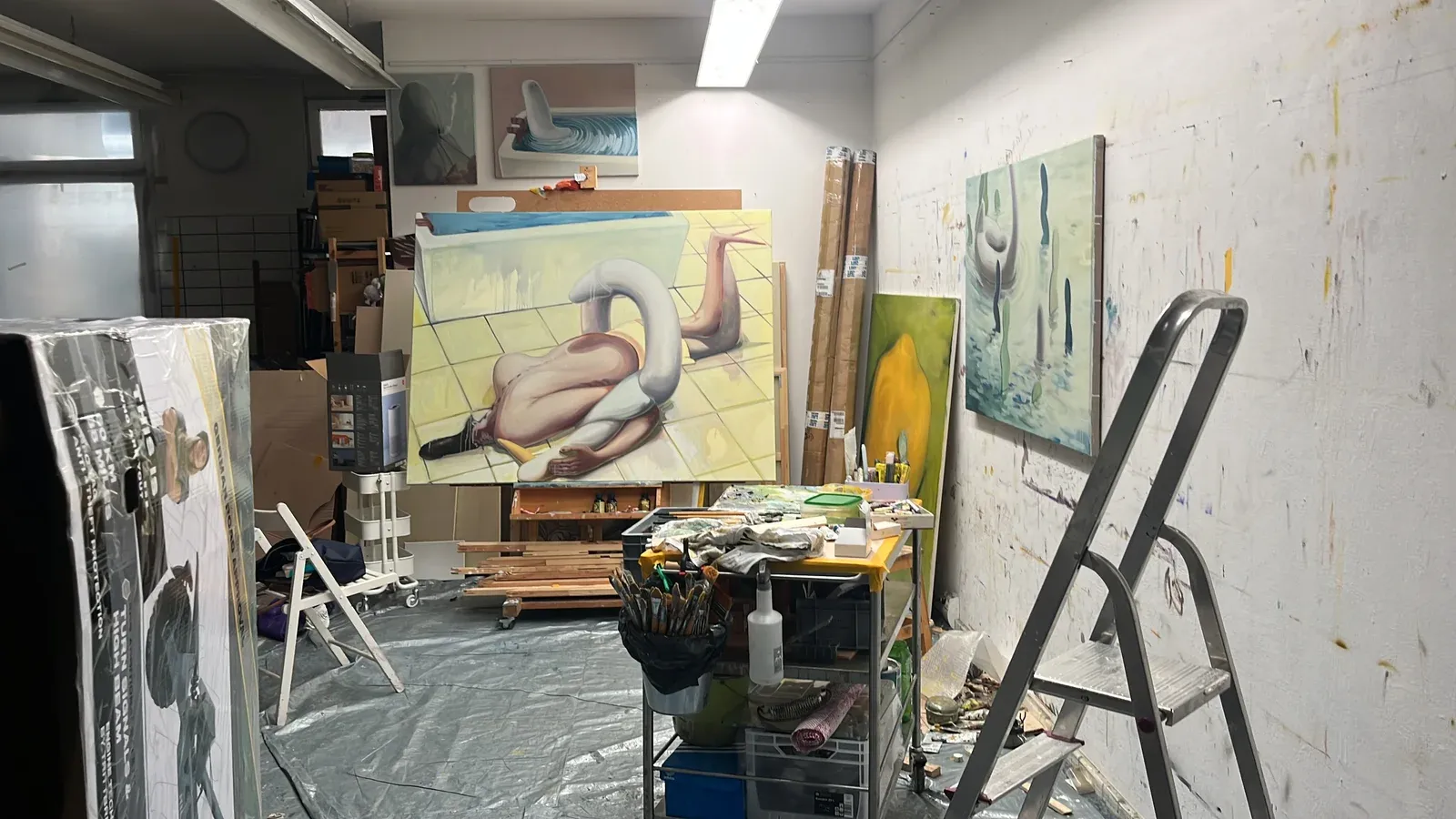 Studio interior of Jeehye Song showing large figurative oil painting on easel, surrounded by tools, canvases and work materials.