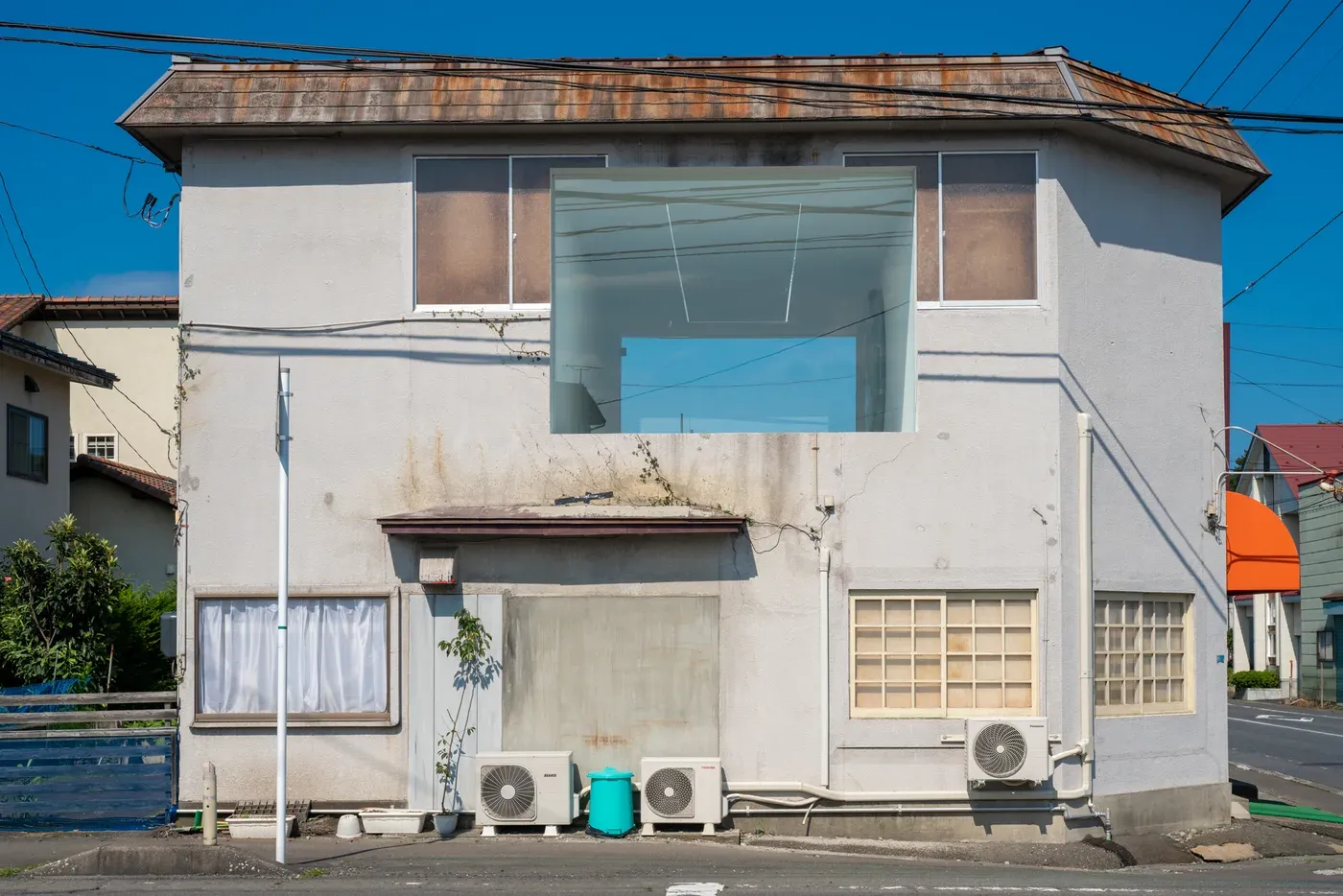 Exterior view of 目 [mé]’s installation space (2020) at Towada Art Center, showing a building façade opened into a luminous interior with a visible staircase and framed architectural intervention.