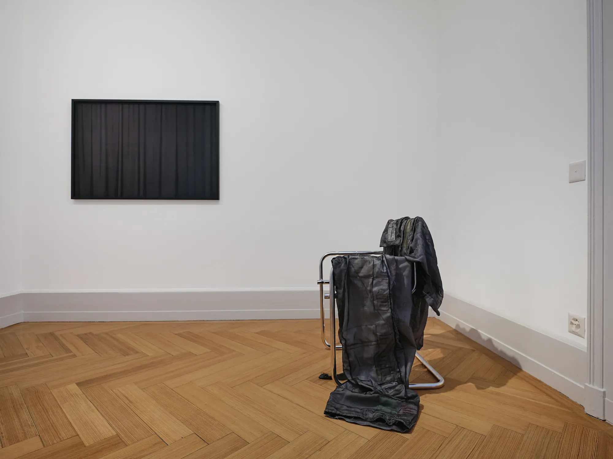 Installation by Marie Matusz featuring a dark jacquard textile wall work and draped black garments over a metal chair in the exhibition “Stitches: A Haunted House and Other Ghost Stories”, Villa Bernasconi, 2026.