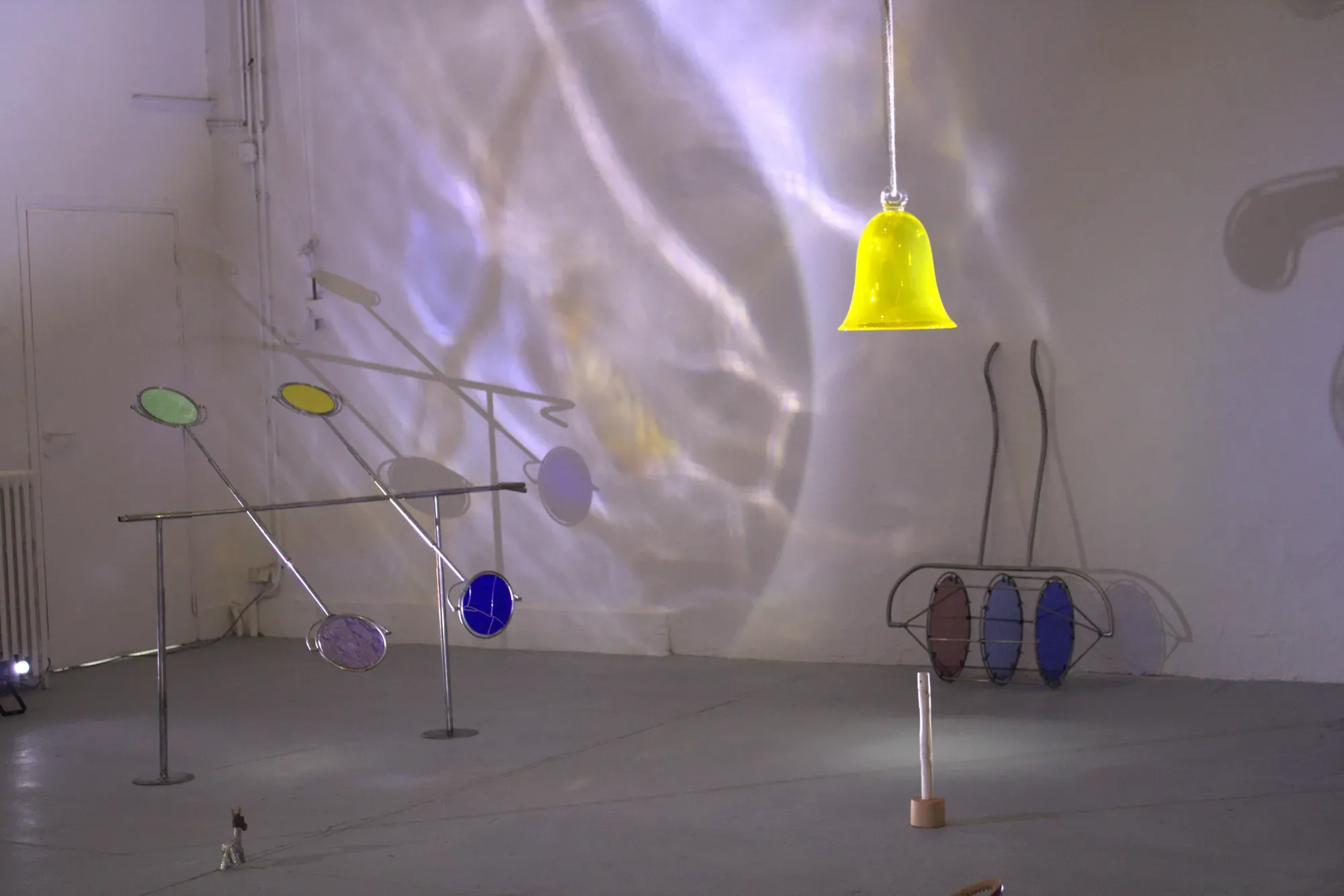 Romane Charlot, ÇA TOURNE, 2024. Installation view with suspended yellow blown glass element and colored glass discs mounted on steel structures projecting light and reflections. Steel, glass, tin. Beaux-Arts de Paris.