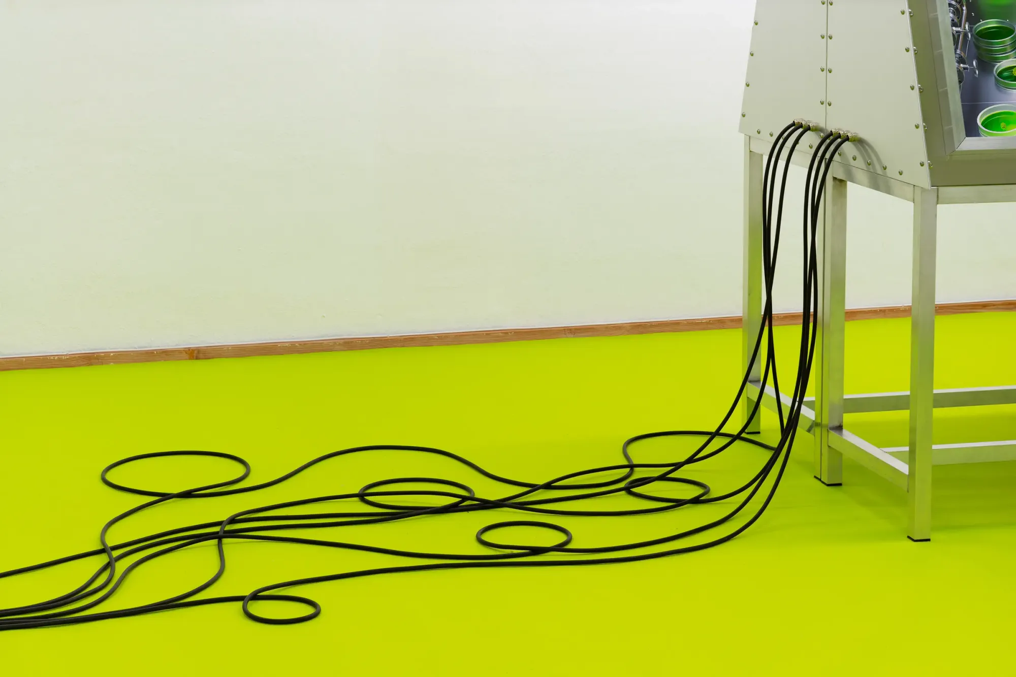 Black cables trailing from metal console across bright neon green floor, forming loose loops and lines against empty gallery wall, minimal installation detail from Stine Deja Micro Management Viborg Kunsthal Denmark
