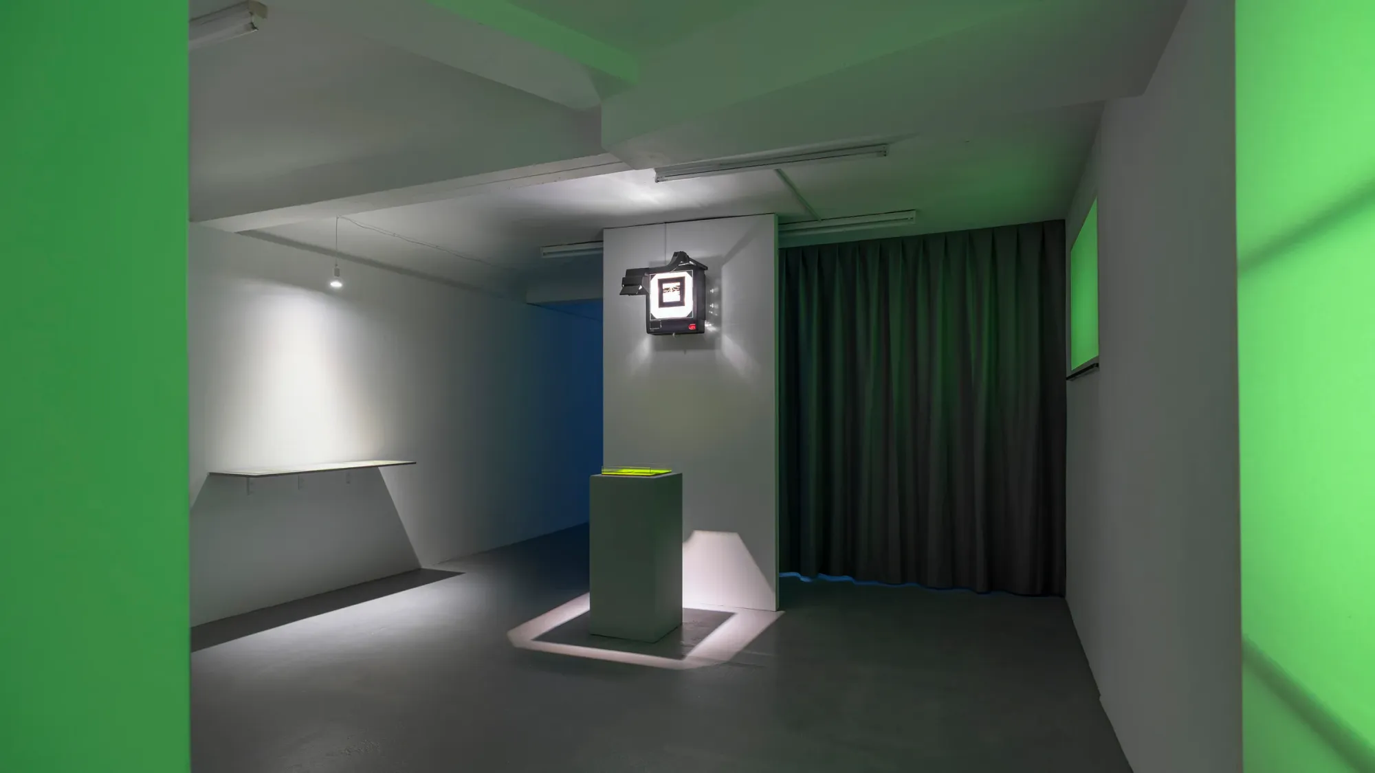 Gallery installation with green light, pedestal displaying translucent green work, vintage CRT monitor mounted on wall, curtain separating space, Kaya & Blank Bloom basis Frankfurt 2026 exhibition view