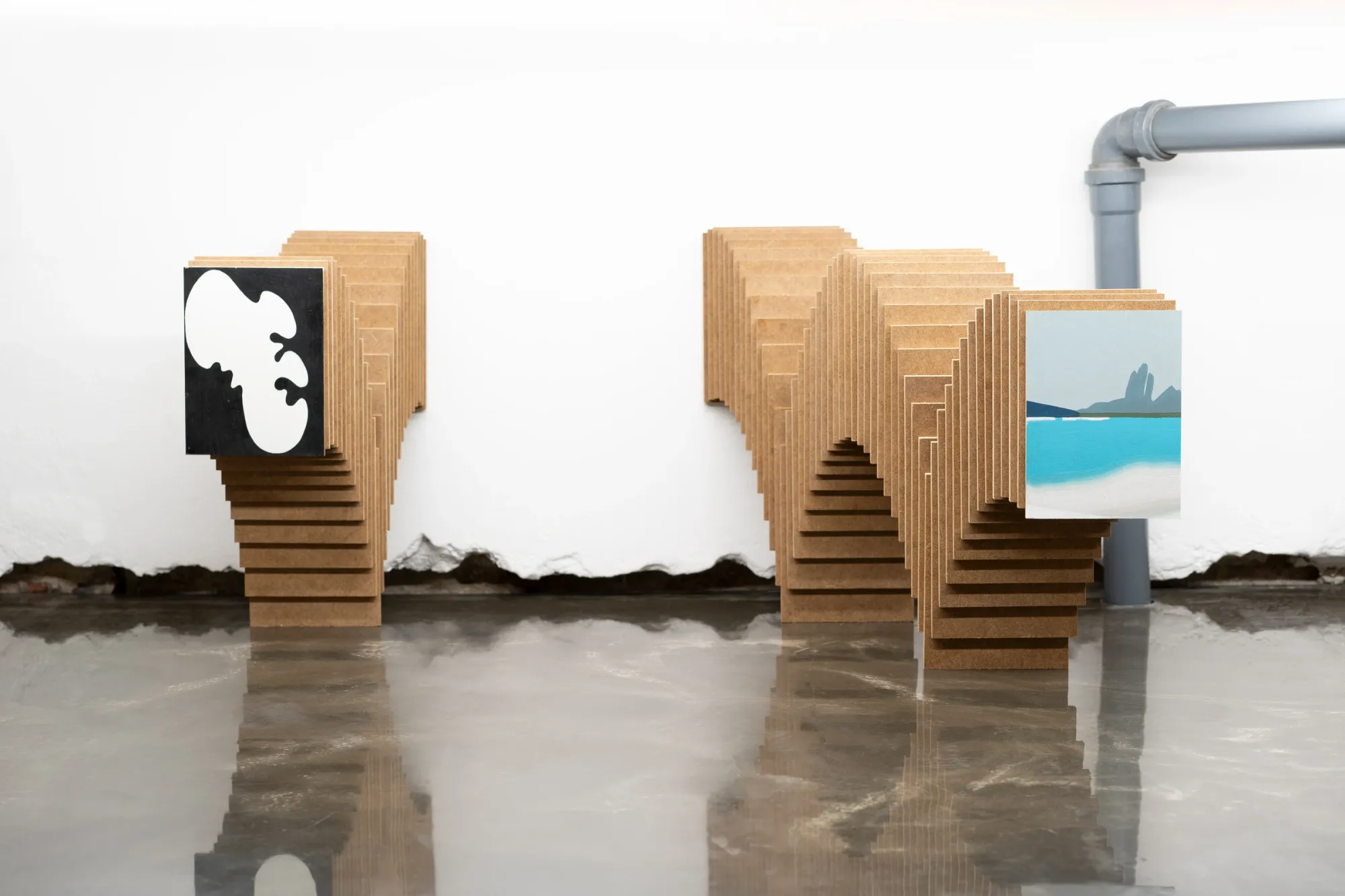 Installation view of Paul Riedmüller at SINK Gallery featuring modular stacked wooden structures displaying small paintings in a reflective floor space