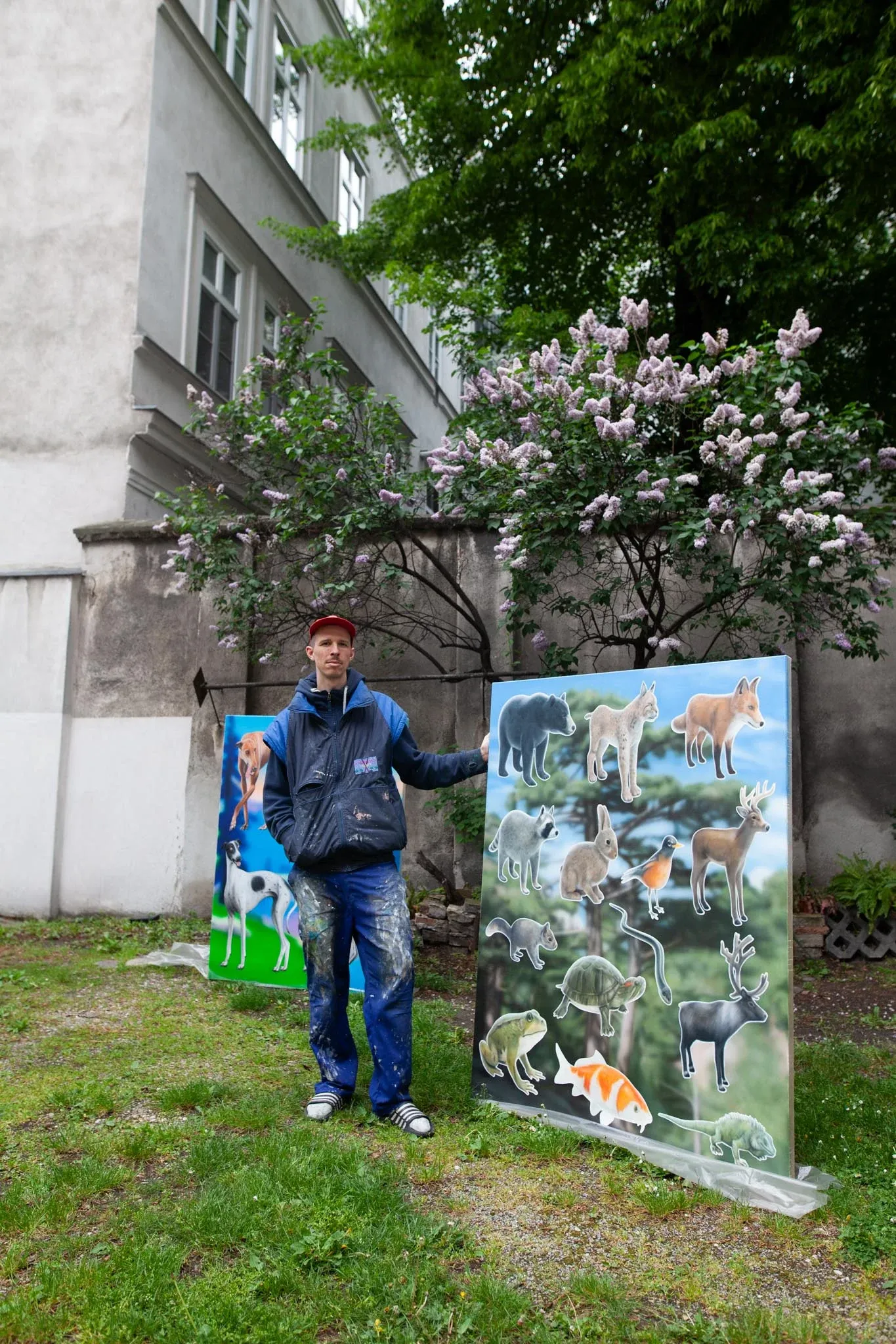 Artist Paul Riedmüller standing outdoors next to large contemporary paintings featuring animals on gradient backgrounds, informal studio portrait in Vienna