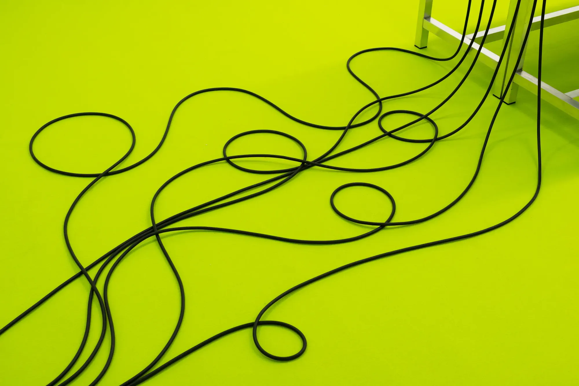 Black cables forming looping lines across bright neon green floor, creating graphic pattern and contrast within installation environment, detail from Stine Deja Micro Management Viborg Kunsthal Denmark
