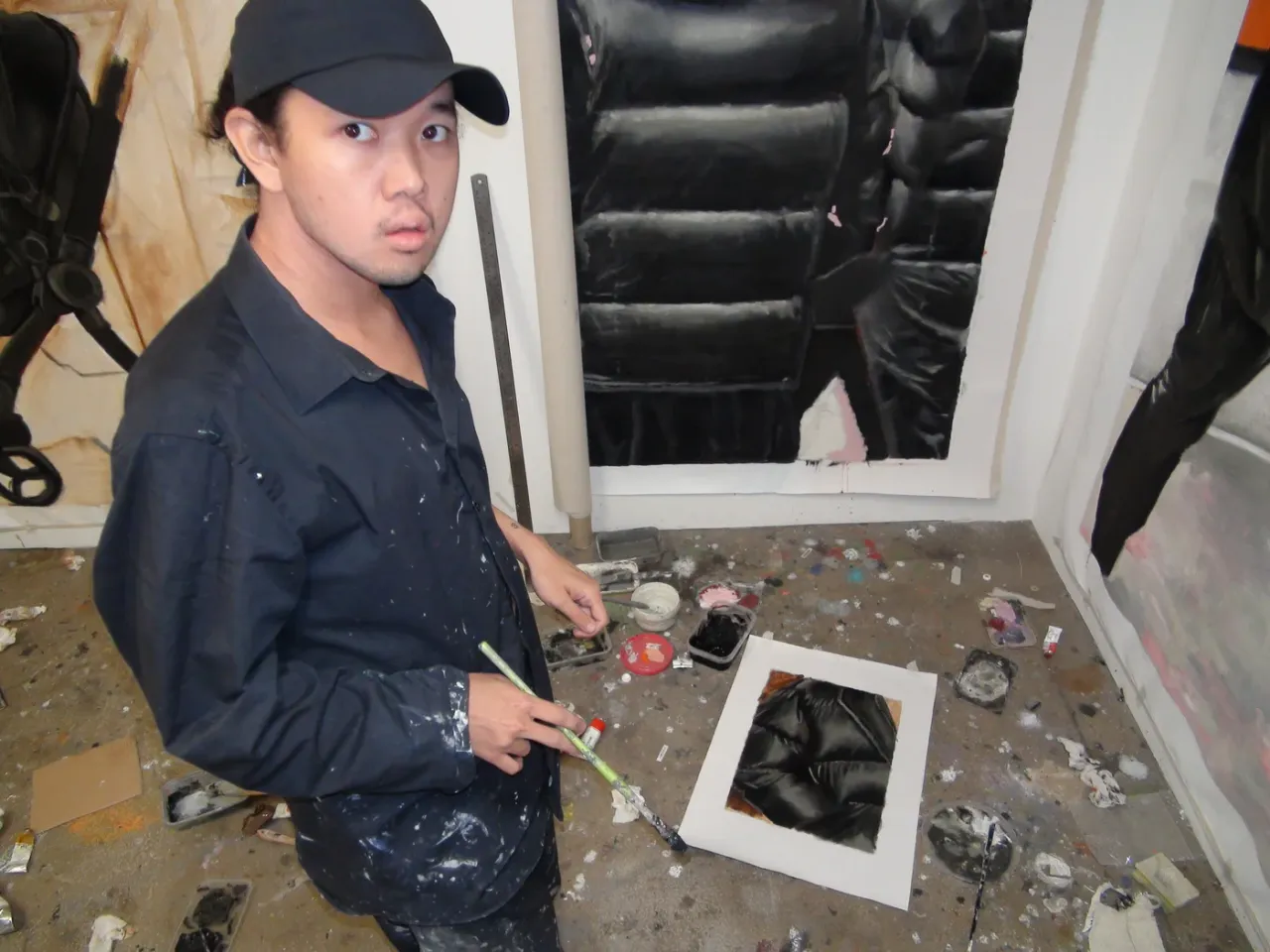 Artist Yutaro Inagaki holding a brush in his studio beside a large puffer jacket painting on the wall.